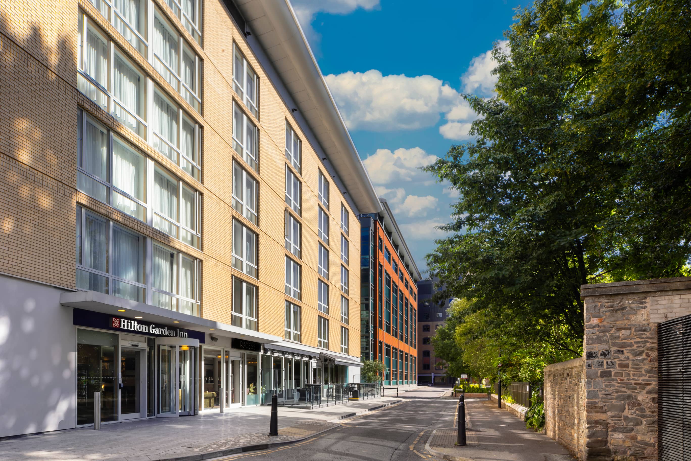 Exterior of Hilton Garden Inn Bristol with pale brick facade and tree-lined street.