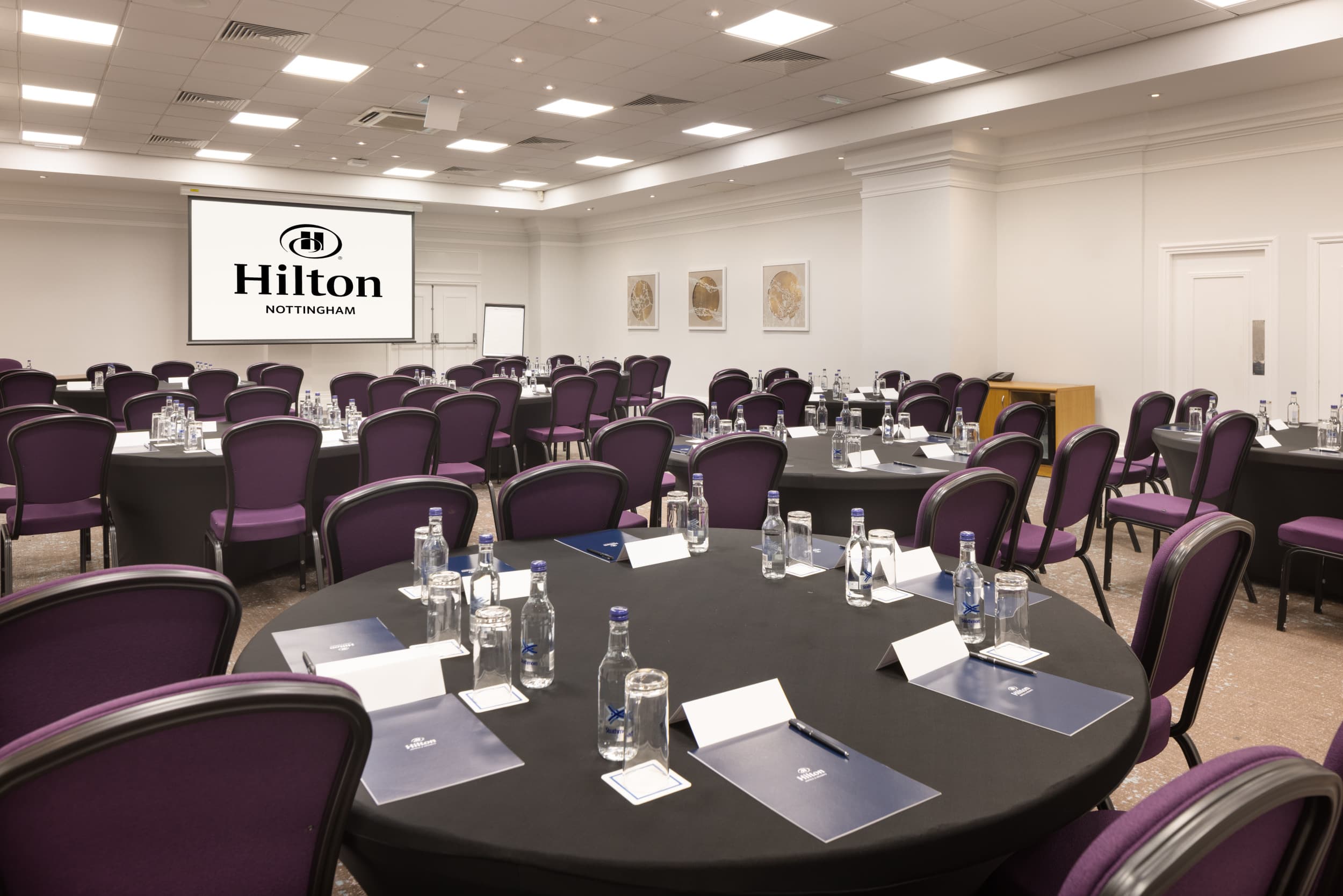 Conference room at Hilton Nottingham set with round tables and purple chairs.