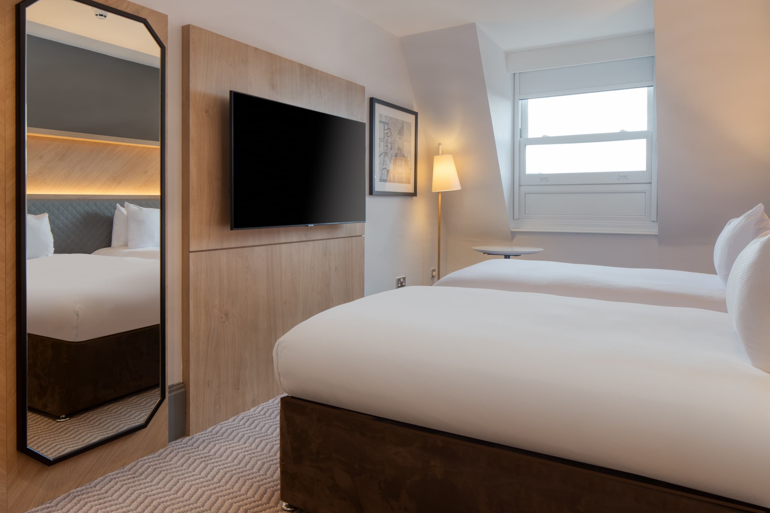 Twin hotel room with wall-mounted TV, floor mirror and sloped ceiling window at Hilton Nottingham.