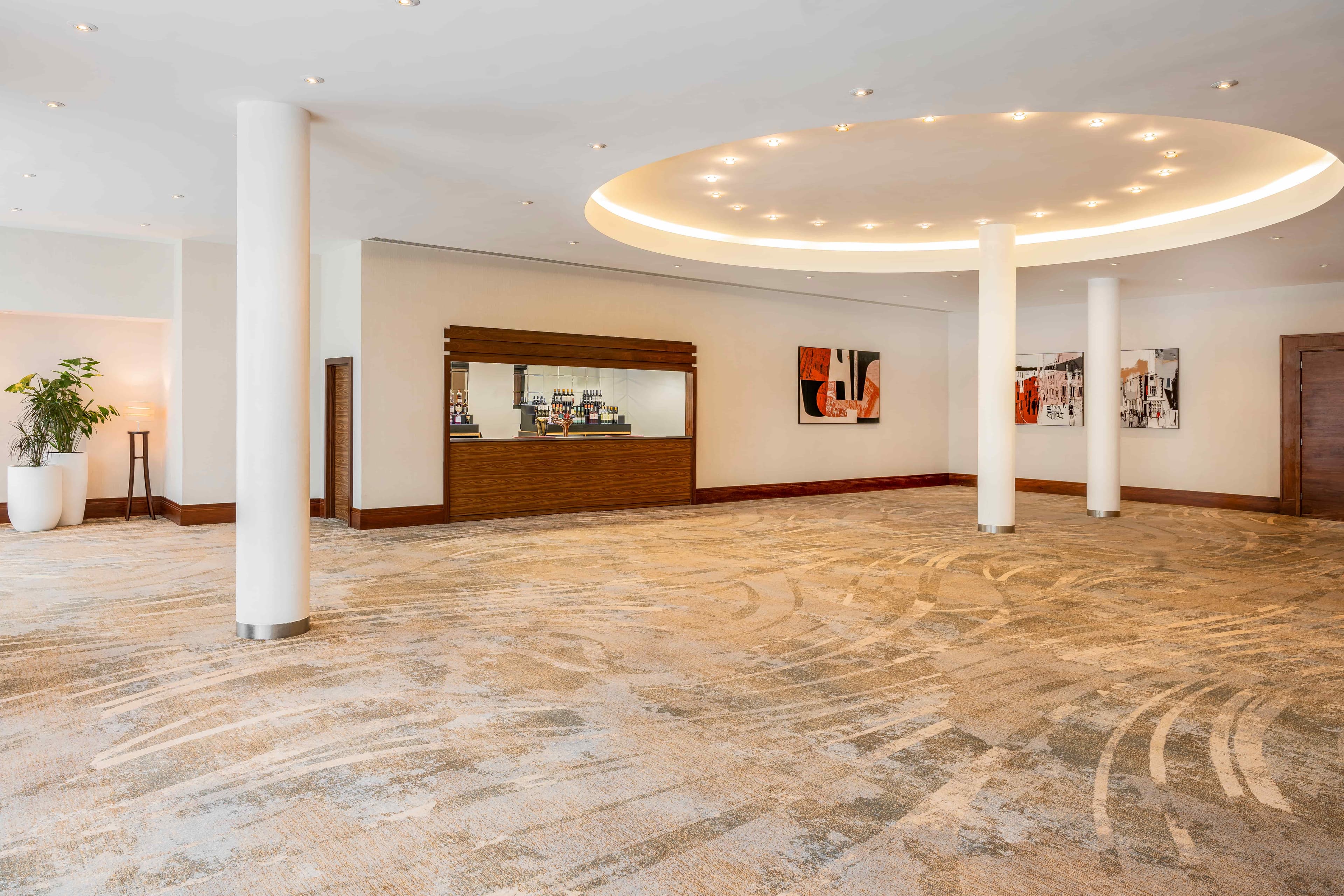 Spacious empty function room with a bar unit, patterned carpet and circular ceiling feature.