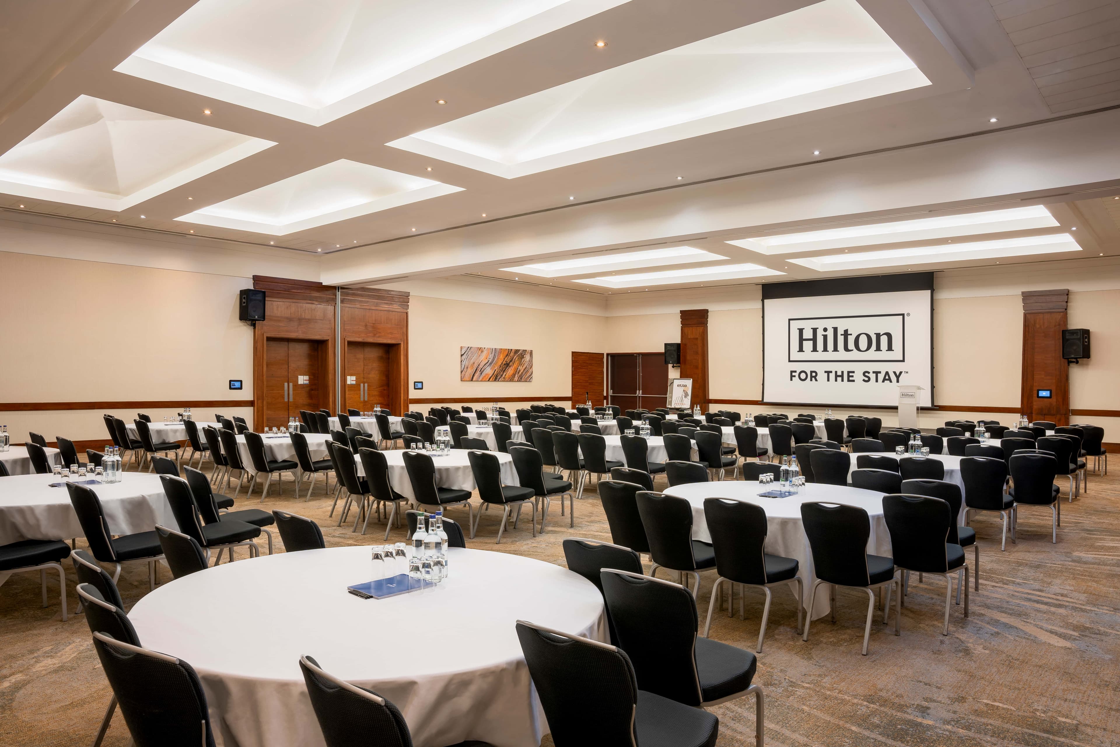 Large conference room at Hilton Reading with round tables, black chairs and a projection screen.