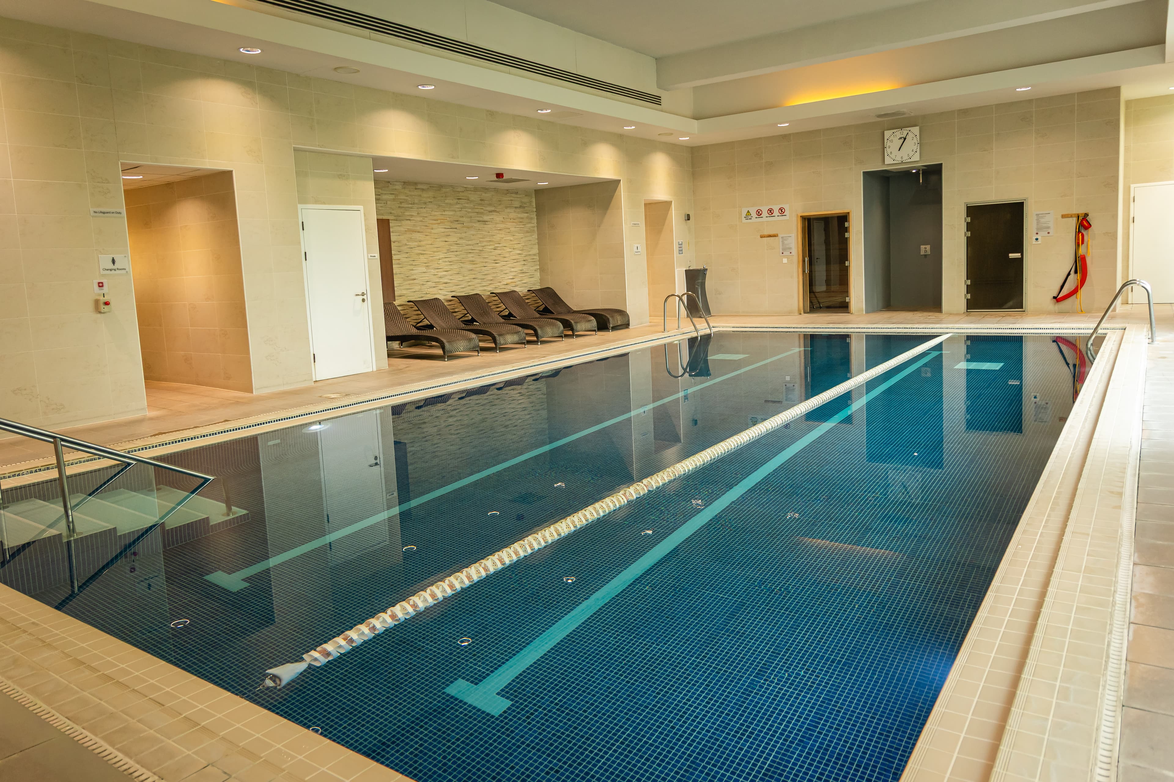 Indoor swimming pool with lane markings, poolside loungers and recessed lighting at Hilton Reading.