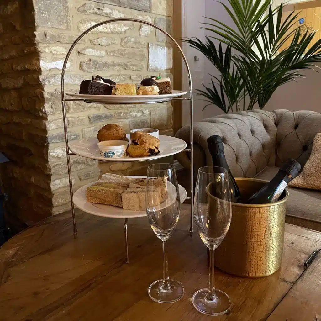 Three-tier afternoon tea stand with scones, sandwiches, cakes and champagne on ice.