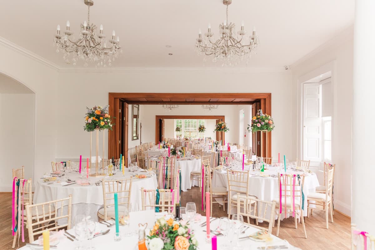 Bright wedding reception room with round tables, colourful candles and crystal chandeliers.