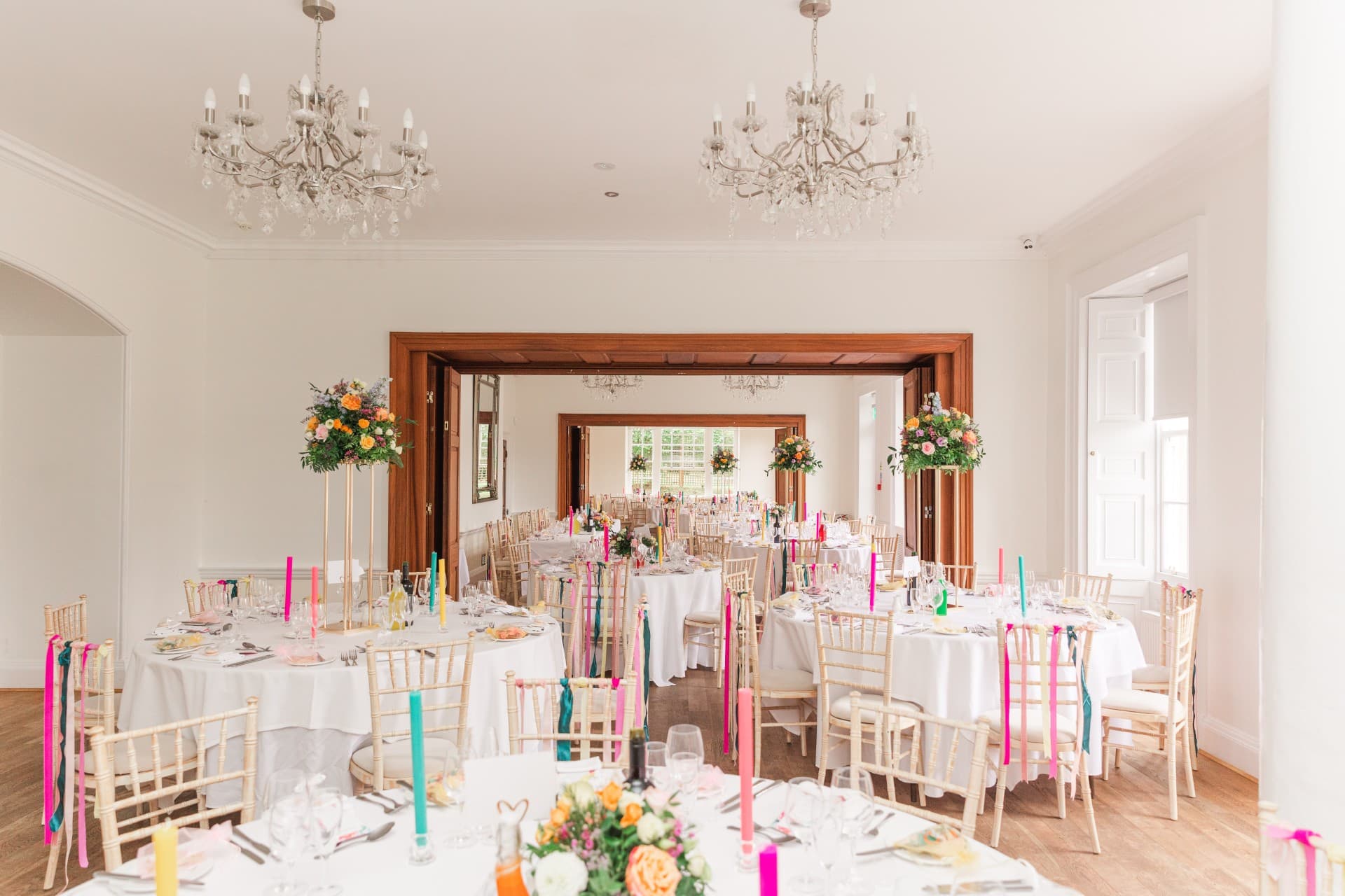 Bright wedding reception room with round tables, colourful candles and crystal chandeliers.