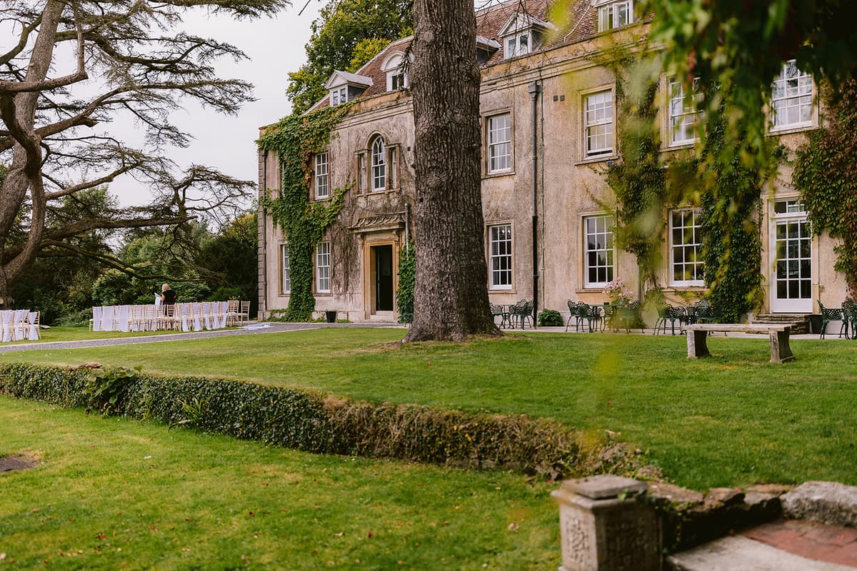 Holbrook Manor's ivy-clad exterior with lawn, outdoor ceremony chairs and garden furniture.
