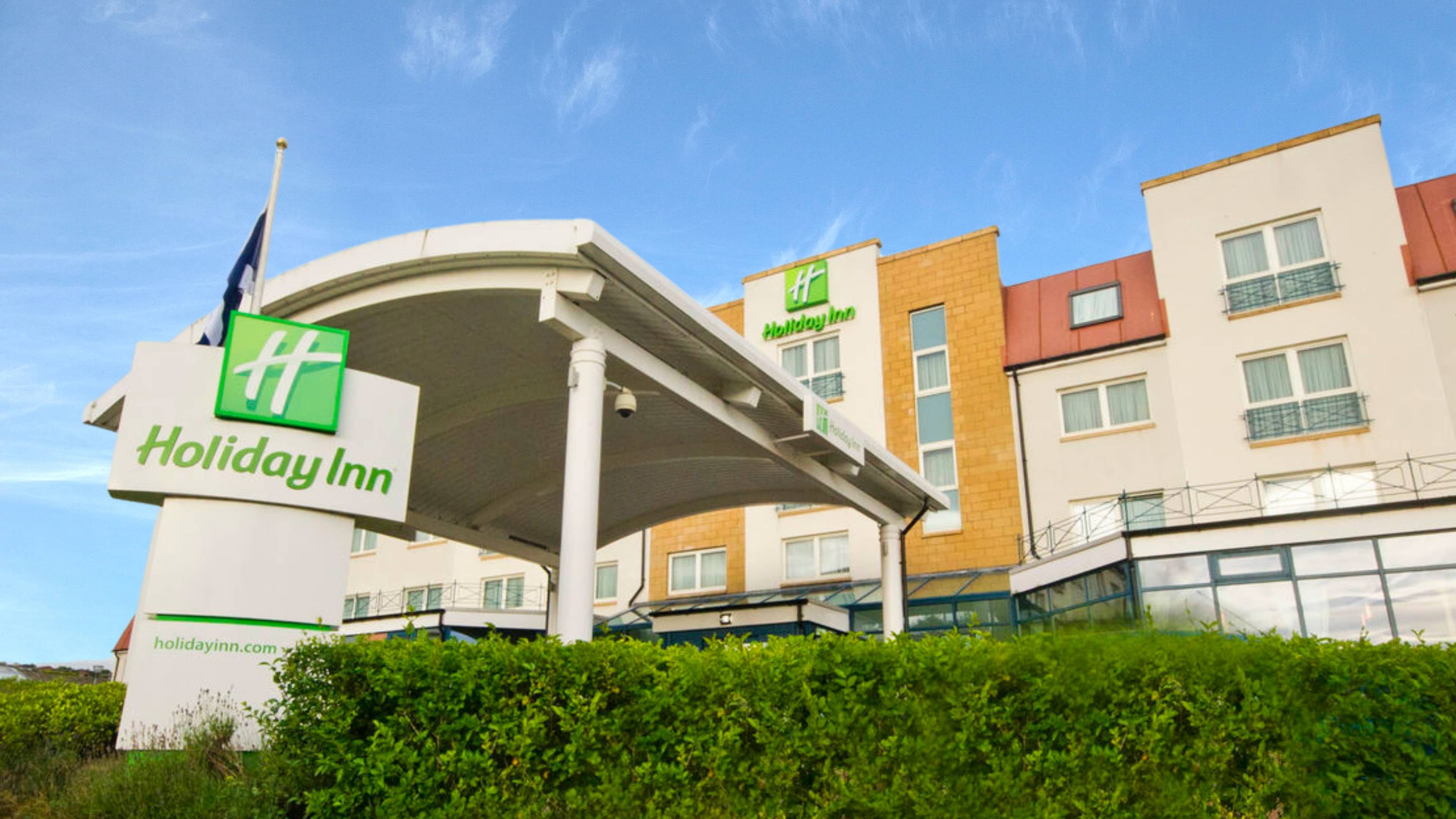 Exterior of Holiday Inn Aberdeen West beneath a blue sky with green hedgerows in front.