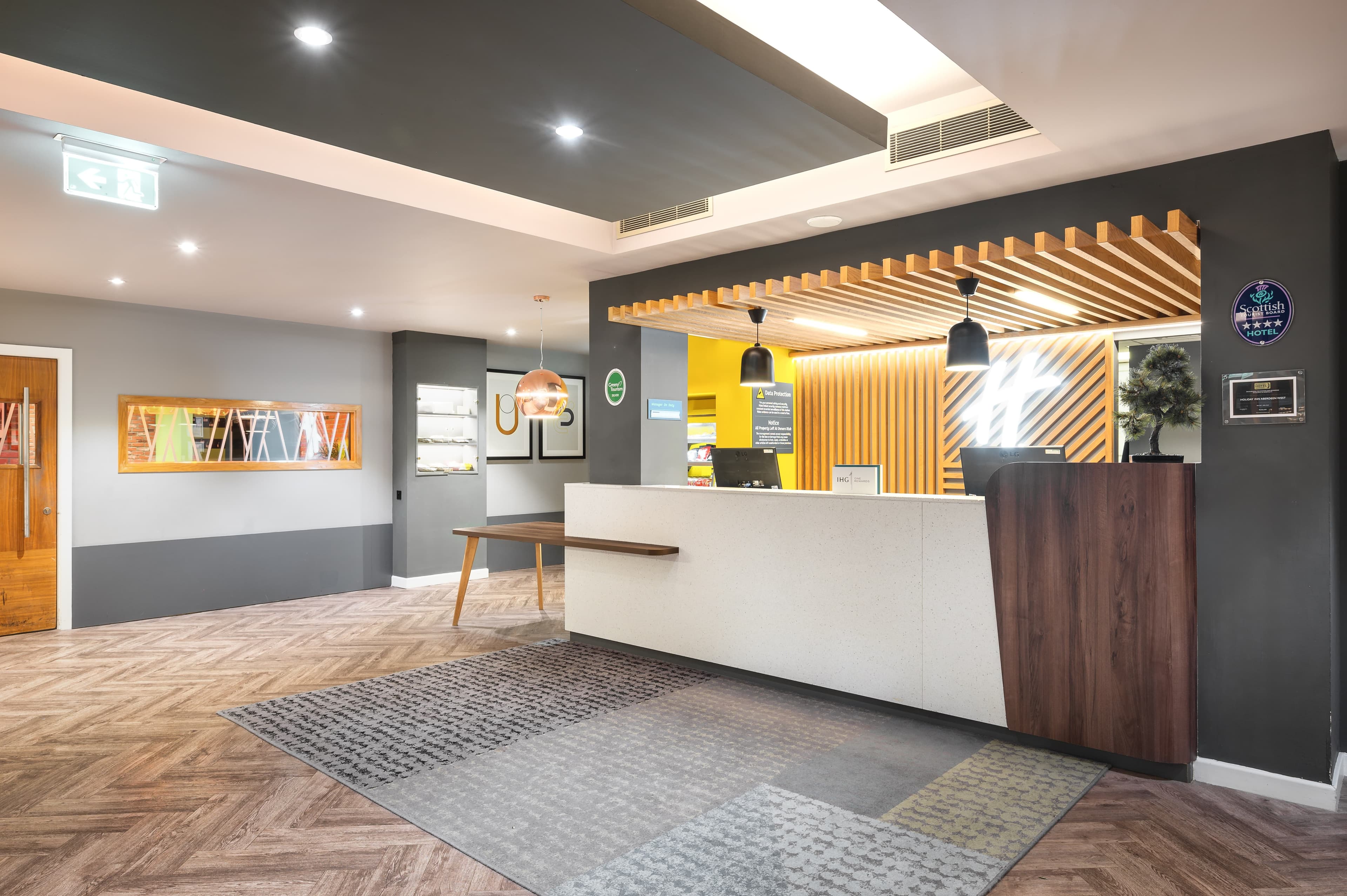 Modern hotel reception desk with wooden panelling, pendant lights and herringbone floor.