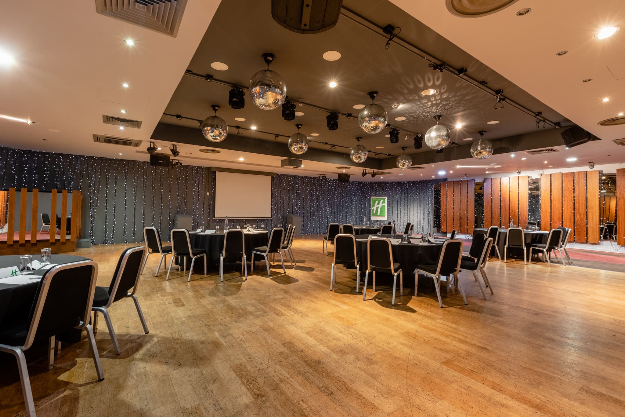 Large function room with round tables, mirrored disco balls and a projection screen.
