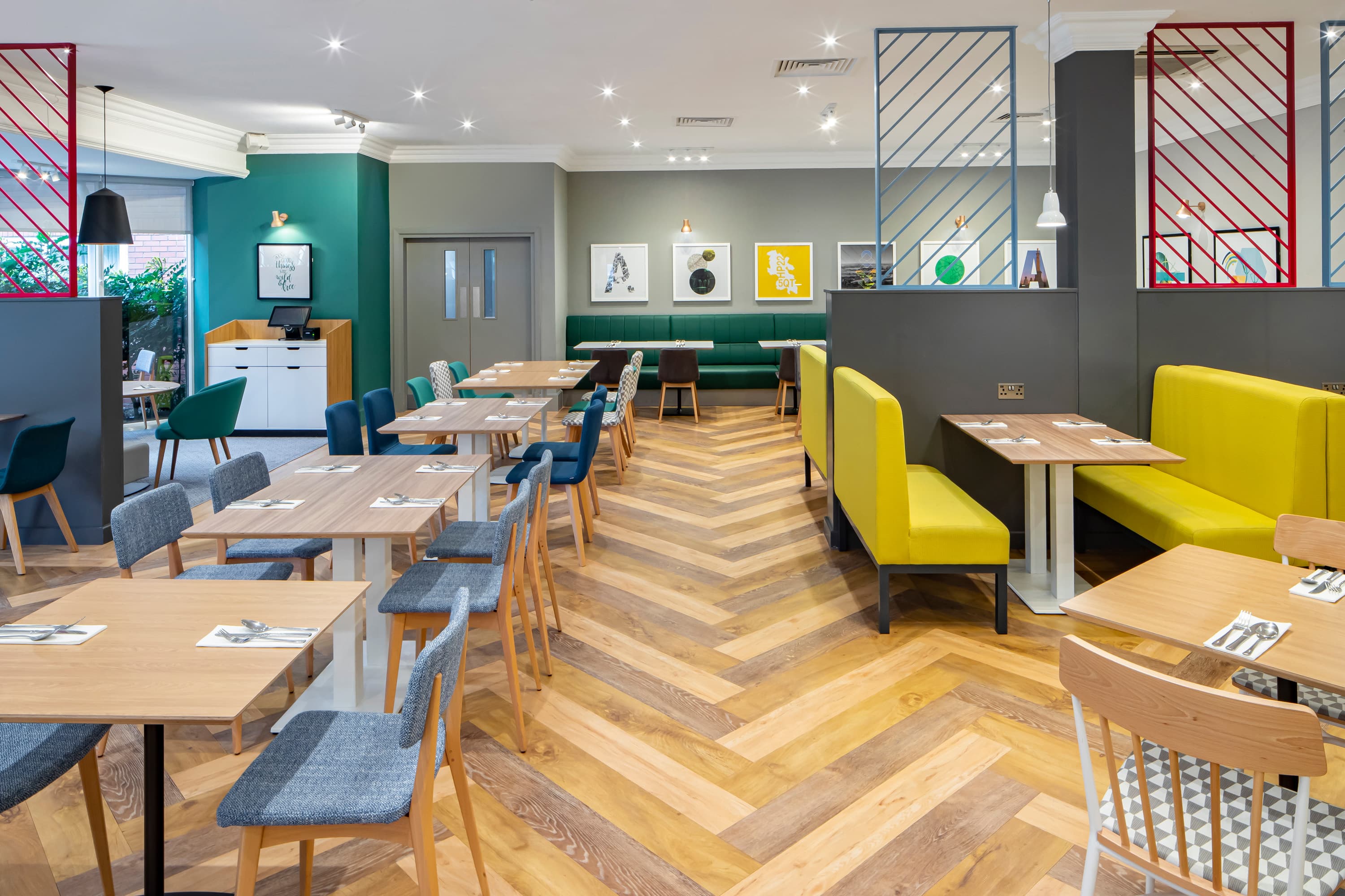 Bright hotel restaurant with herringbone wood flooring, yellow booths and colourful chairs.