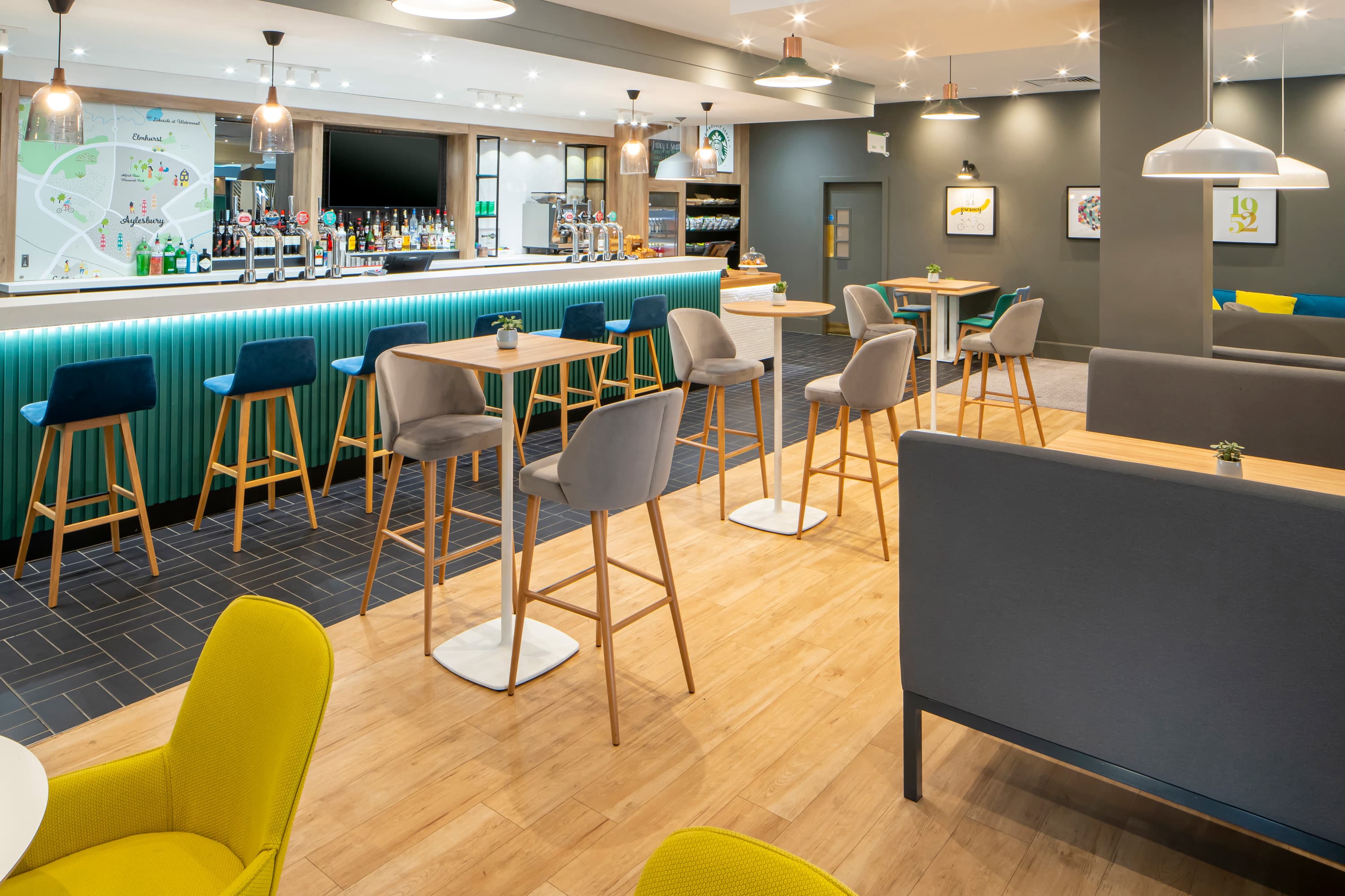 Modern hotel bar area with high stools, pendant lighting and yellow accent chairs.