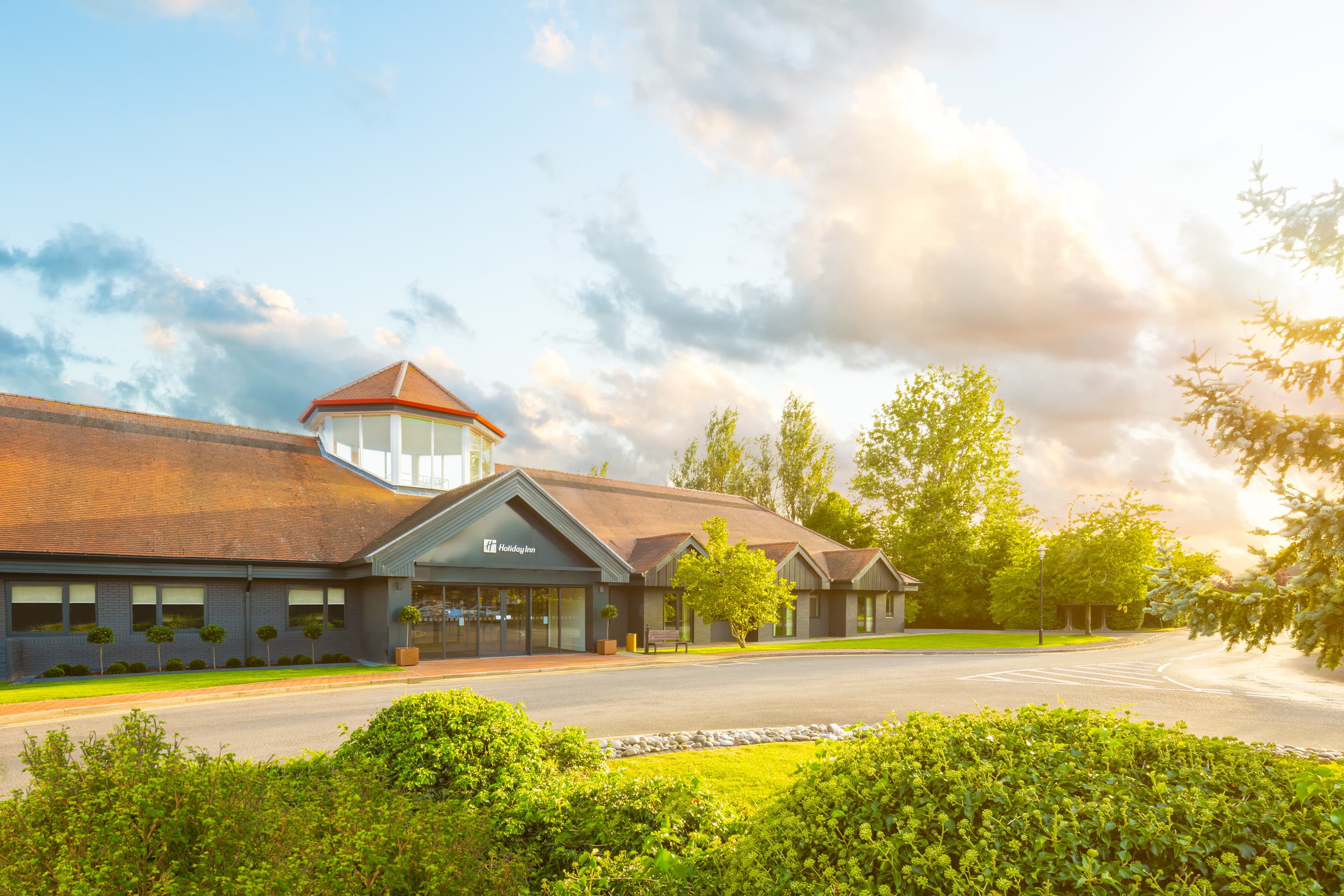 Exterior of Holiday Inn Aylesbury showing the entrance, terracotta roof and surrounding trees.