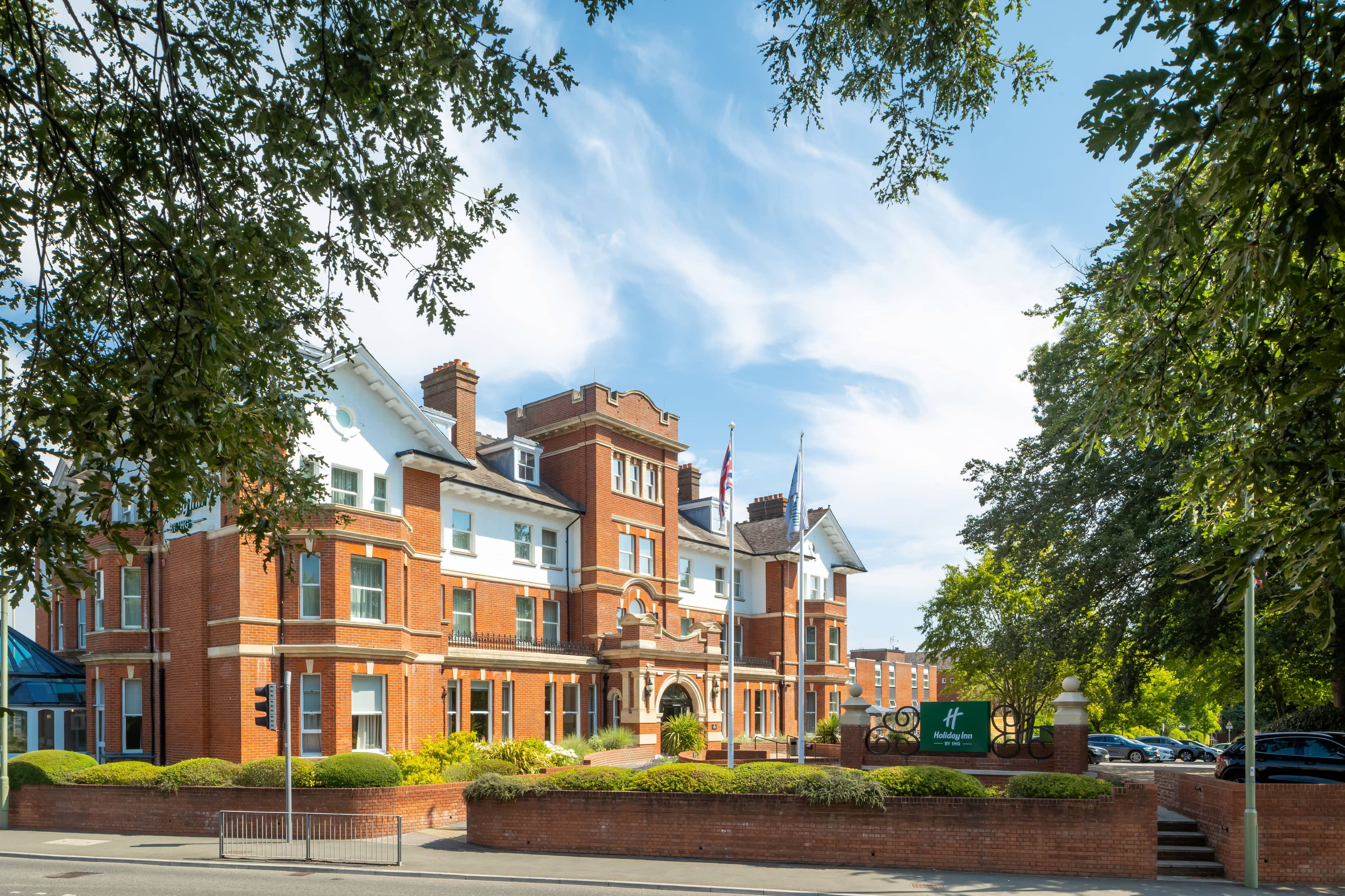 Exterior of the Holiday Inn Farnborough showing its red brick Victorian facade and mature trees.