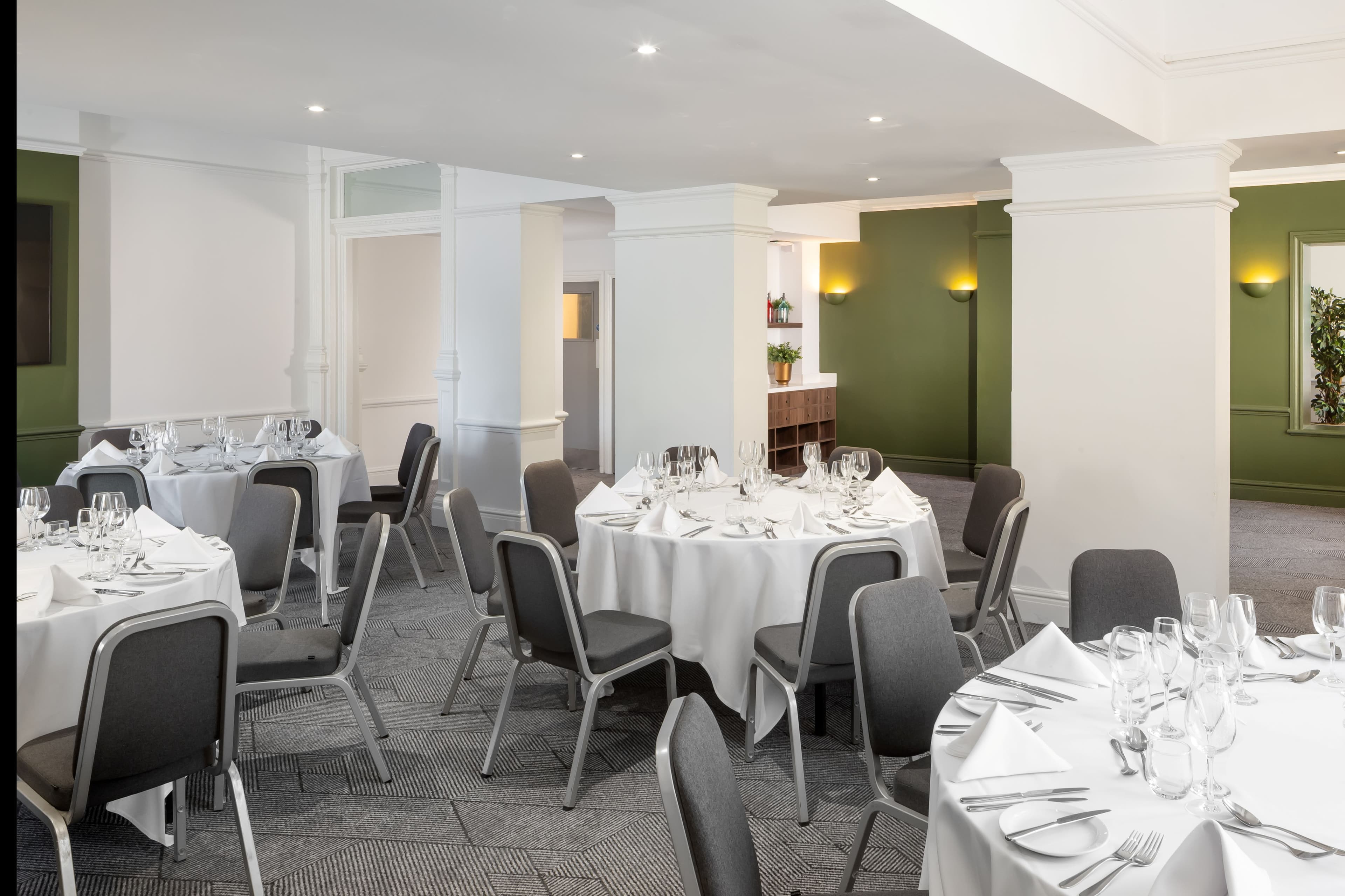 Private dining room with round tables laid for dinner and green panelled walls.