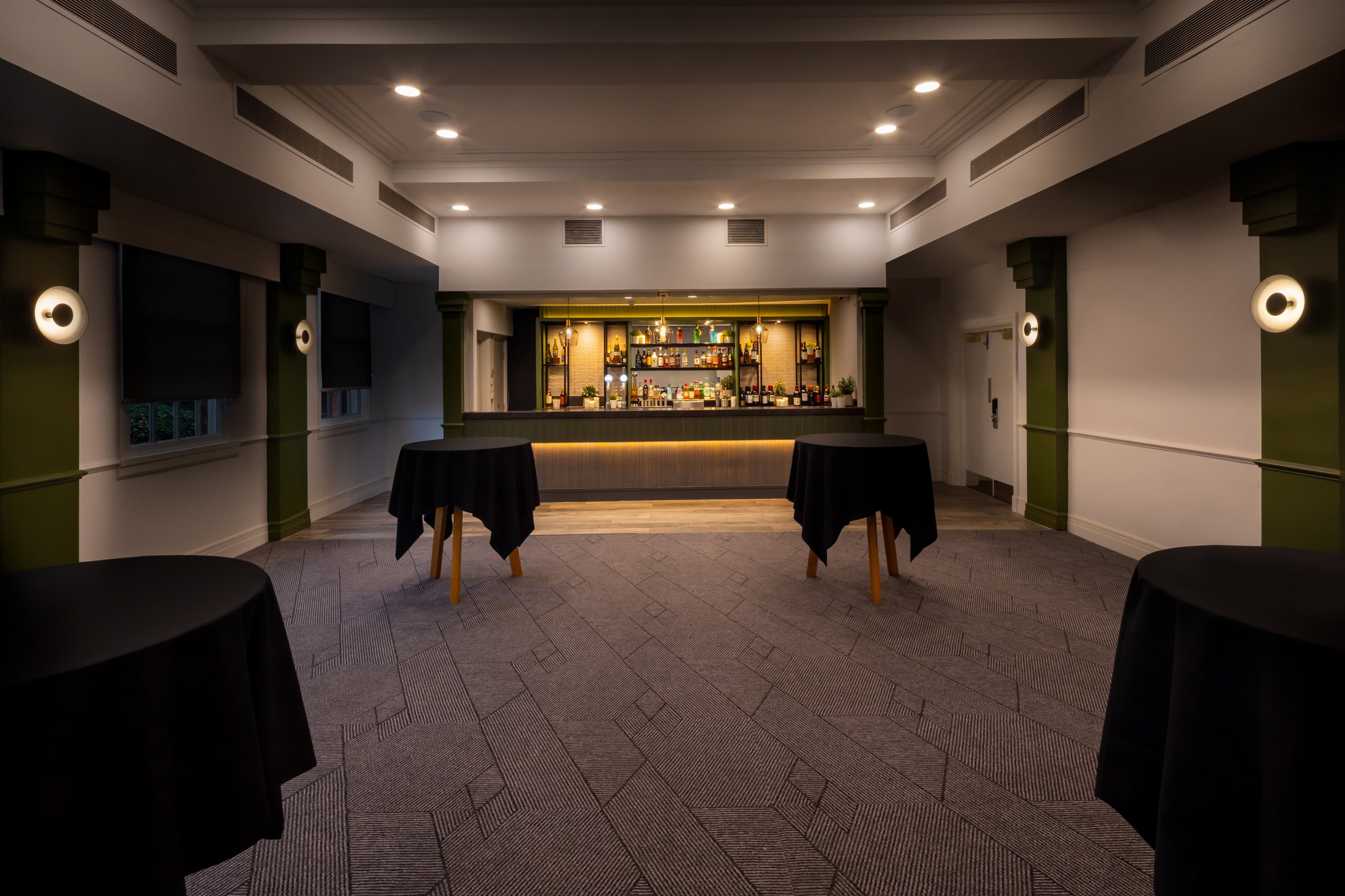 Private function room with a built-in bar, poseur tables and patterned carpet.