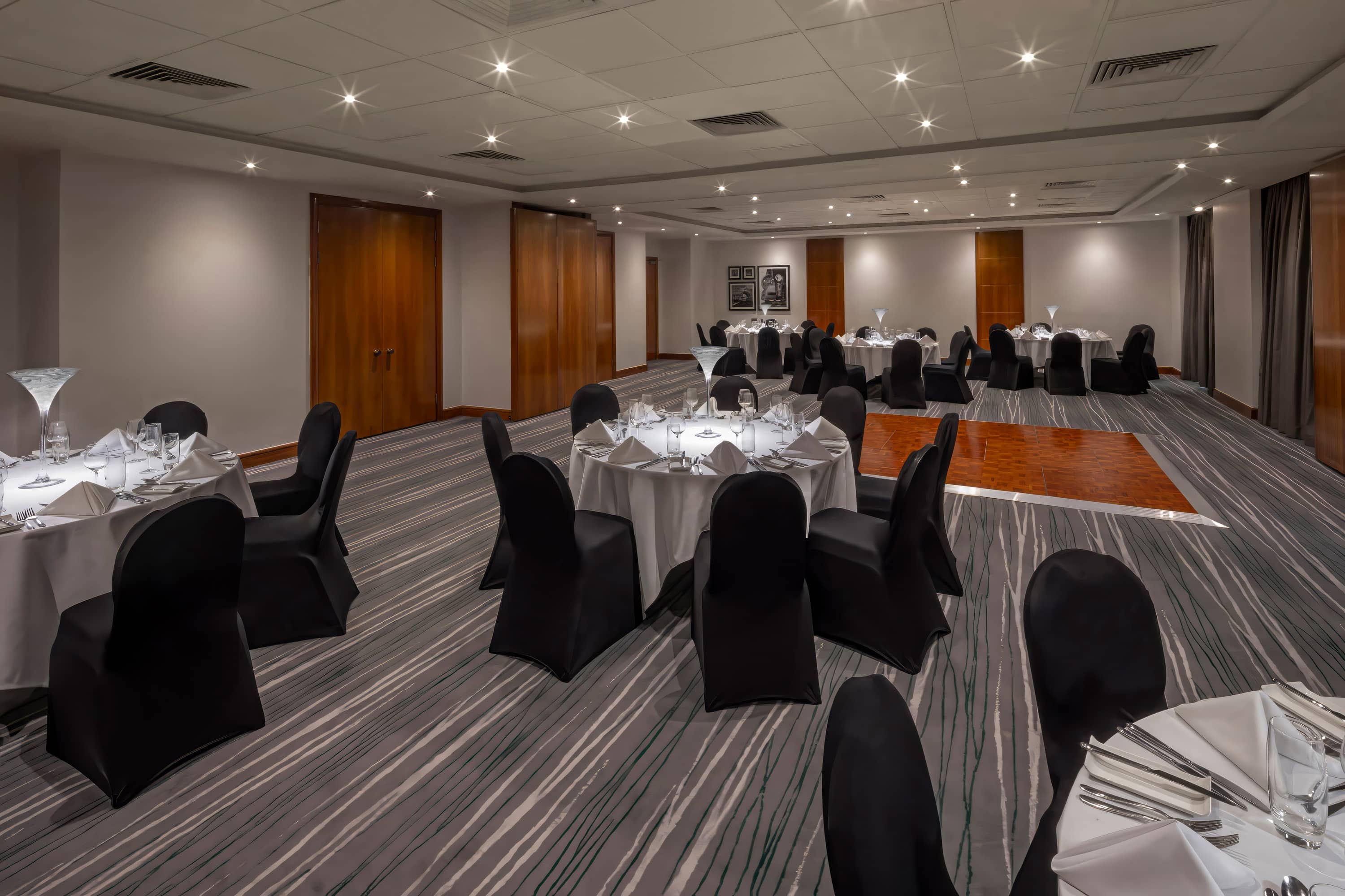 Banqueting room with round tables, black chair covers and patterned carpet at Holiday Inn Gloucester.