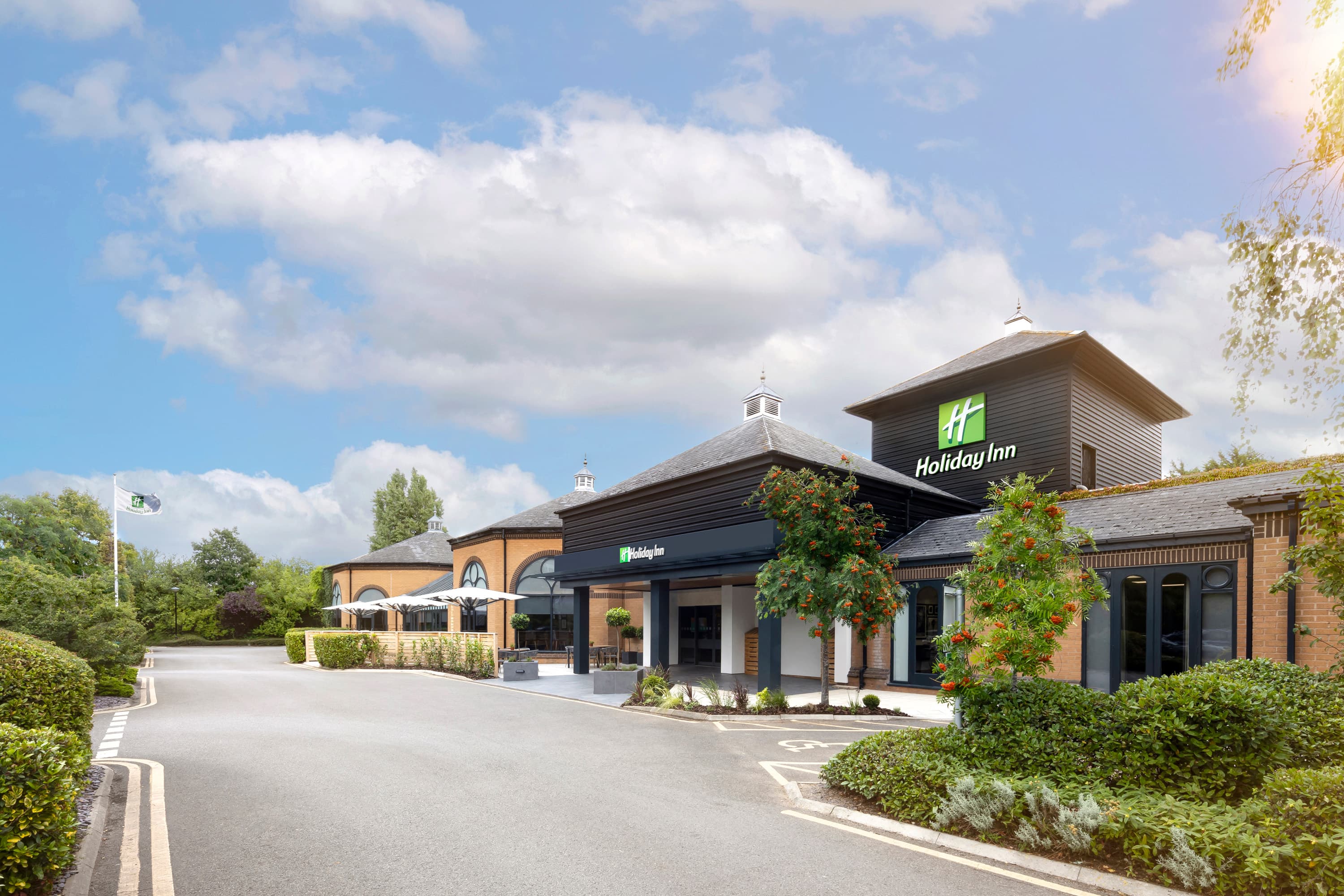 Exterior of Holiday Inn Gloucester Cheltenham on a sunny day with landscaped grounds.