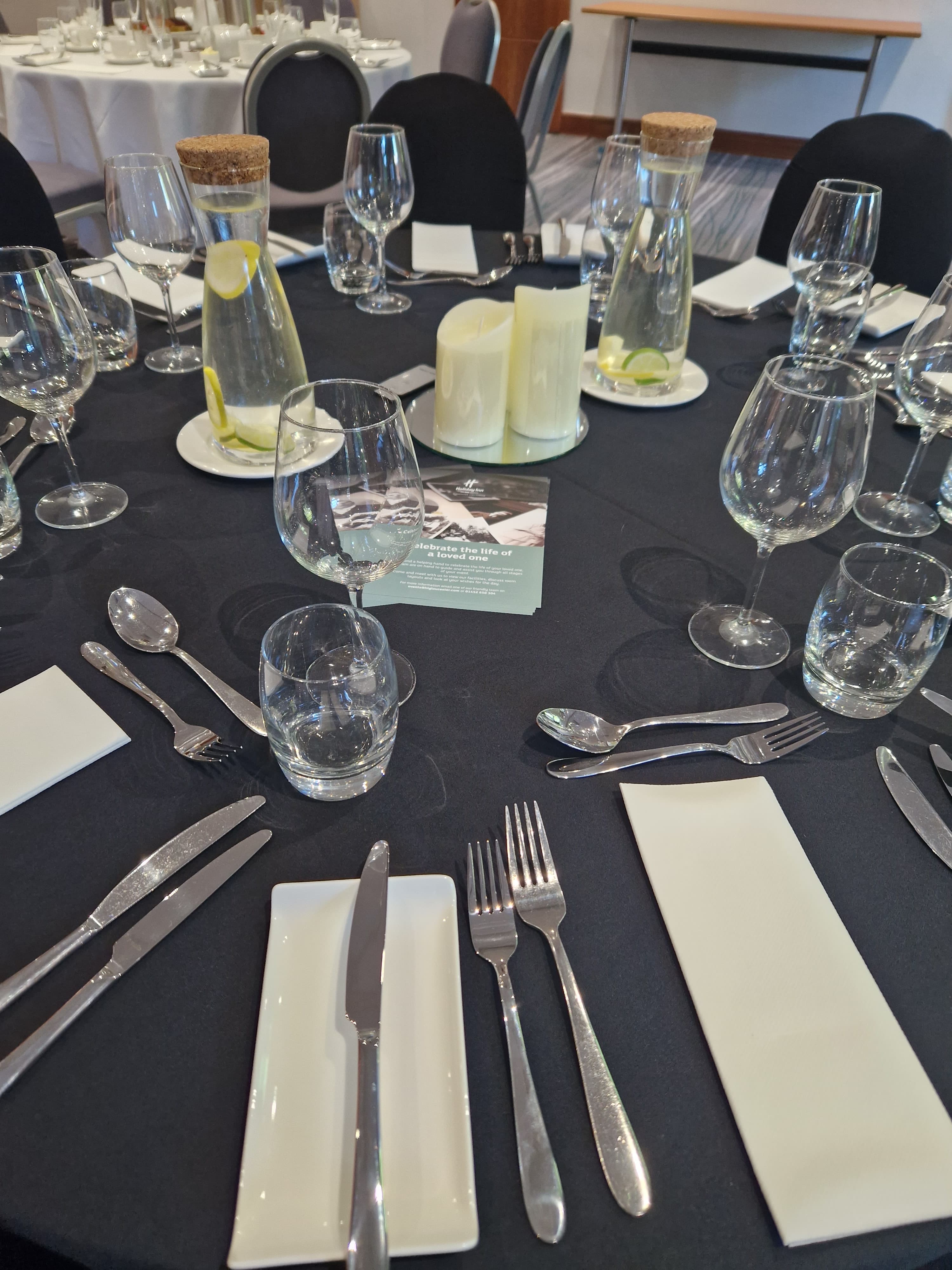 Round banquet table laid with cutlery, glassware and white candle centrepiece.