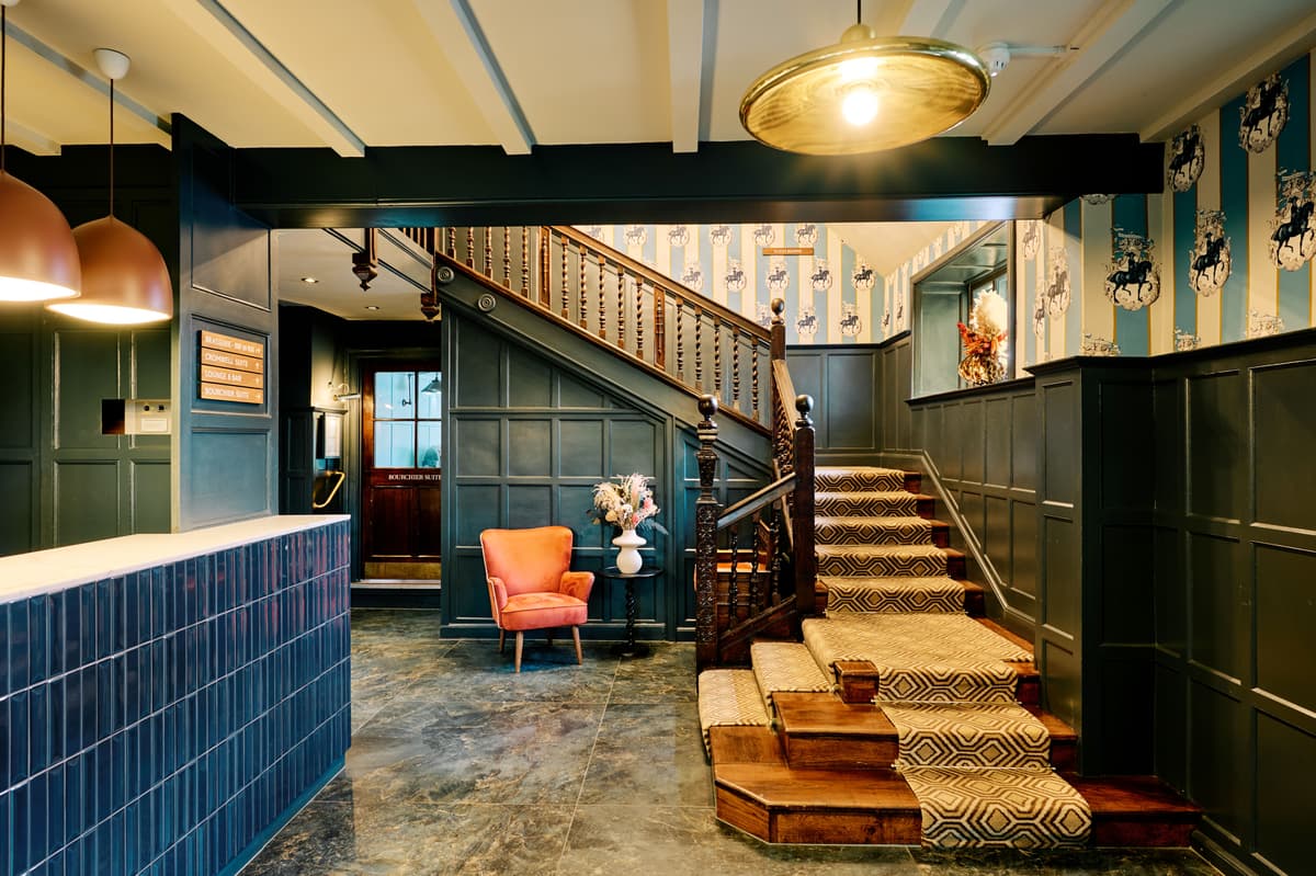 Hotel Cromwell reception area with wooden staircase, patterned carpet runner and blue tiled desk.