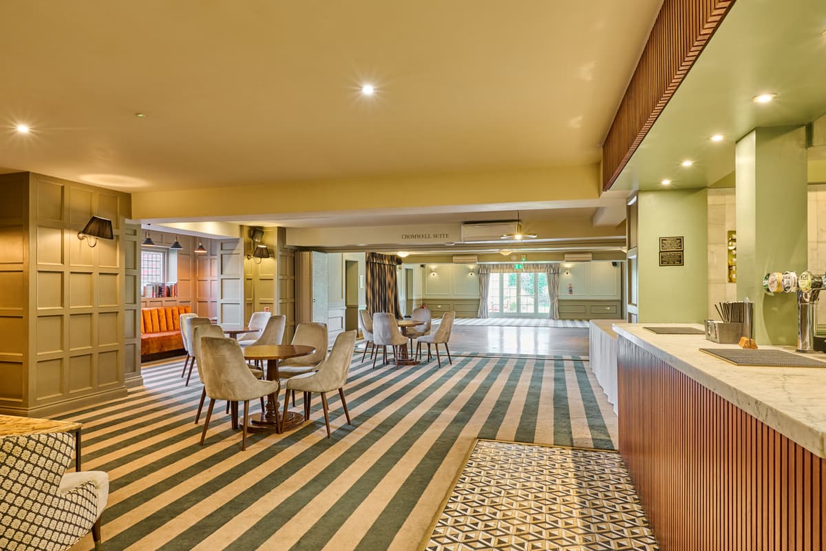 The Cromwell Suite bar area with striped carpet and grey upholstered seating.