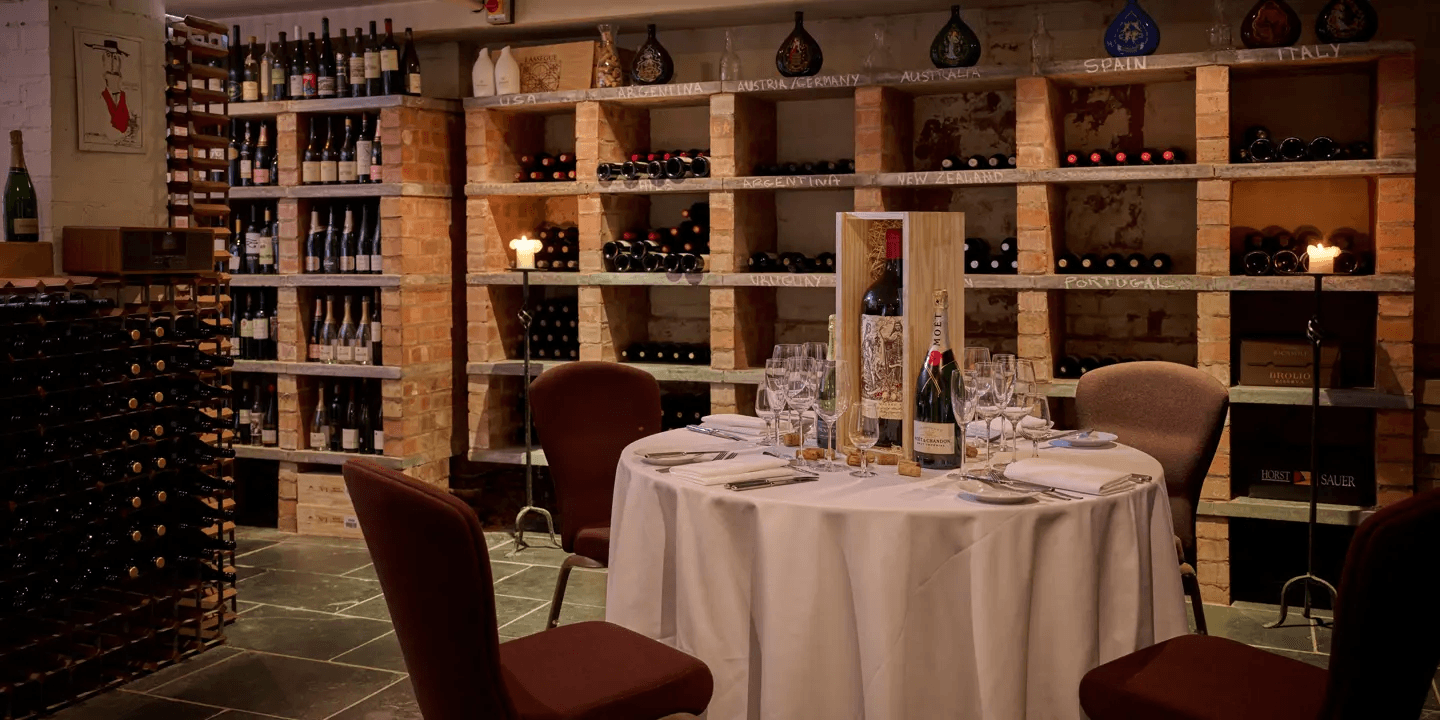 Wine cellar dining room with a set round table surrounded by extensive bottle racks.