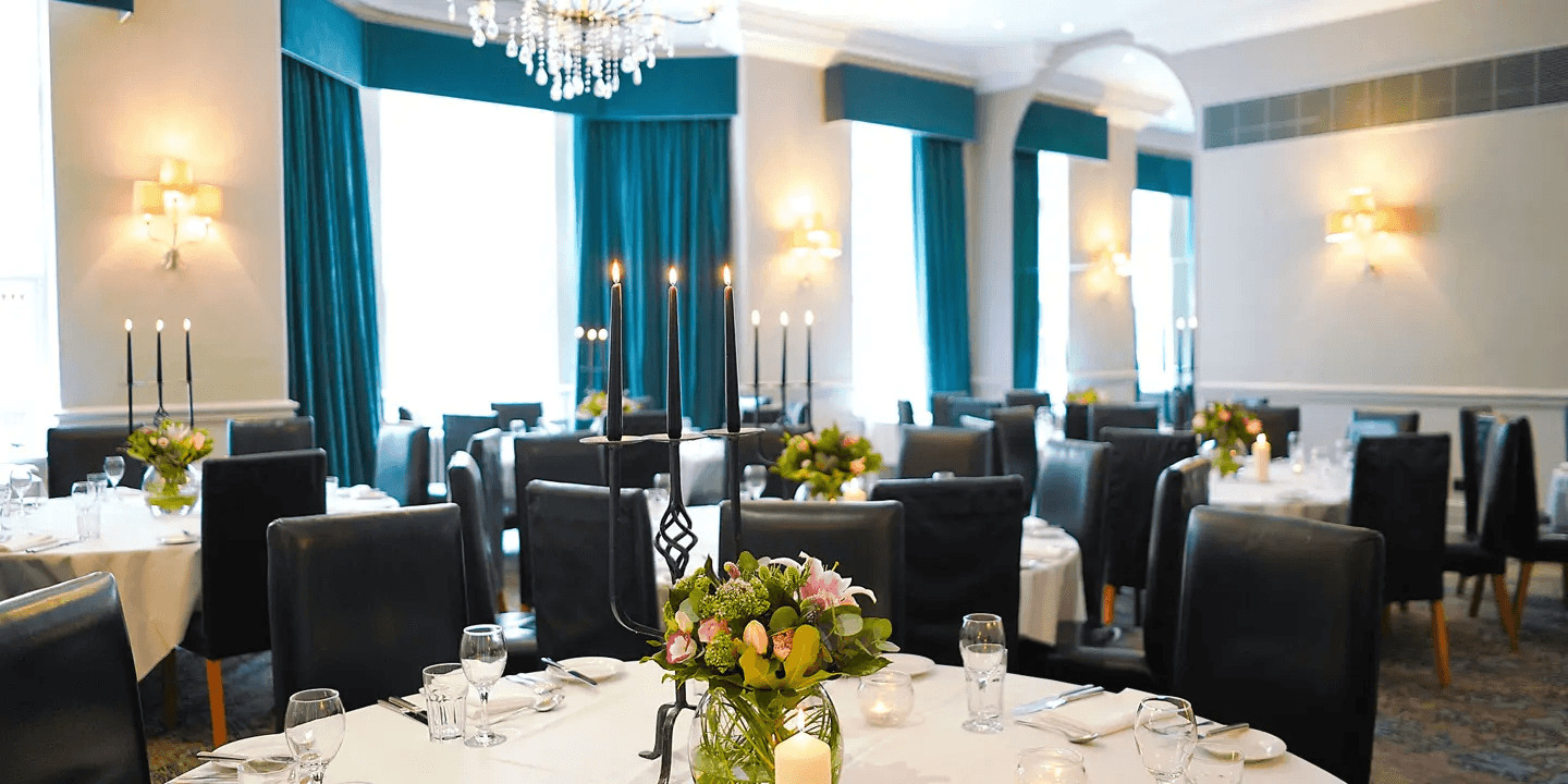 Private dining room with round tables, black candelabras and teal curtained windows.