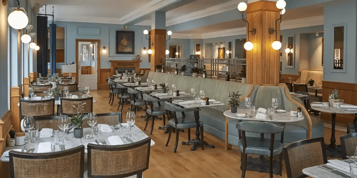 Restaurant dining room with marble tables, rattan chairs and a long upholstered banquette seat.