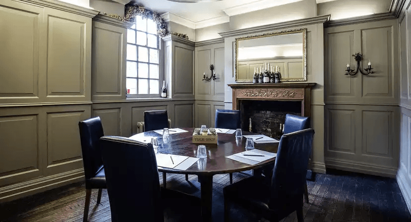 Panelled private dining room with round table, leather chairs and ornate fireplace.