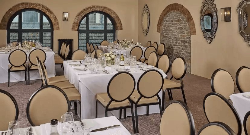 Private dining room with white-clothed tables, round-backed chairs and exposed brick arches.