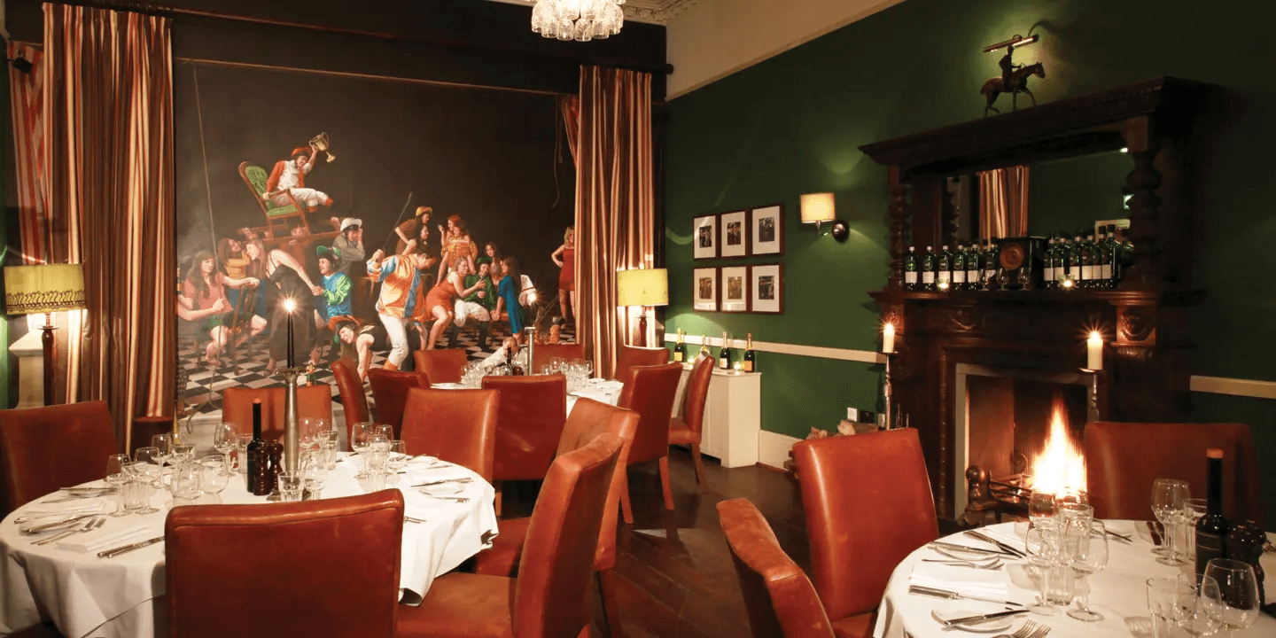 Private dining room with red leather chairs, lit fireplace and large mural painting.
