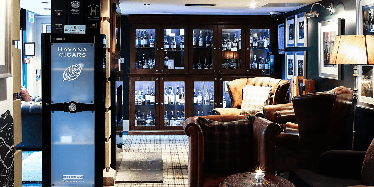 Whisky bar lounge with leather armchairs, backlit spirit cabinets and a Havana cigars humidor.