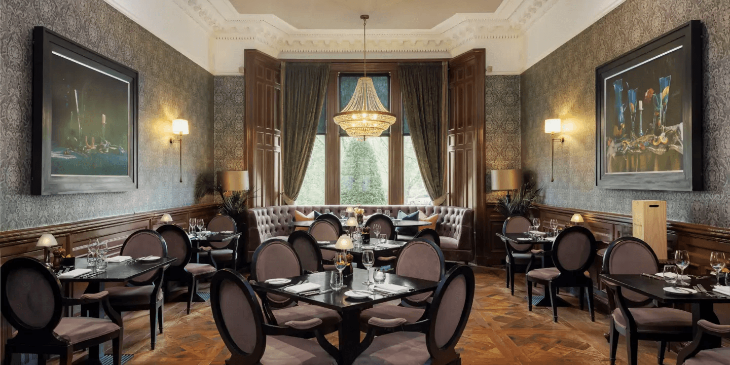 Elegant restaurant dining room with dark wood panelling, patterned wallpaper and a crystal chandelier.