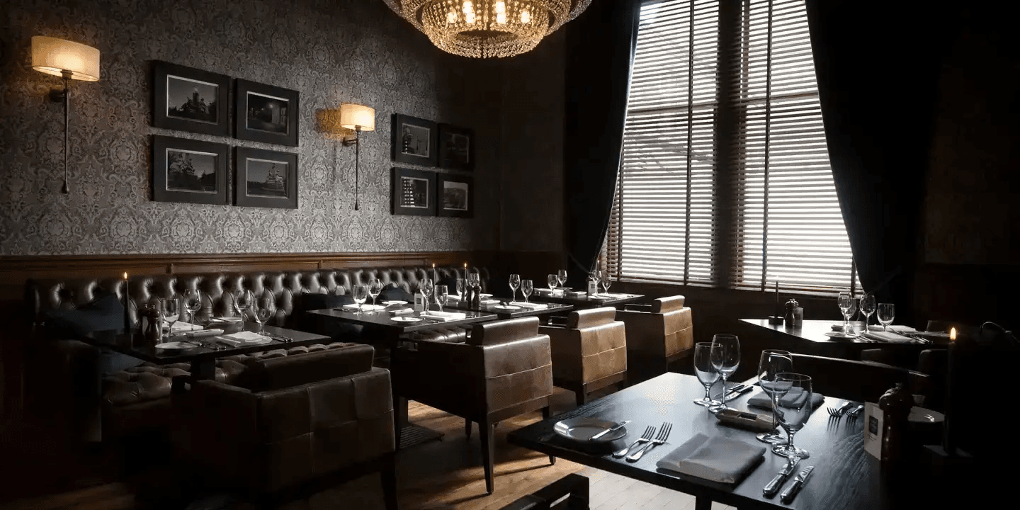 Dimly lit restaurant dining room with leather banquettes, set tables and a crystal chandelier.