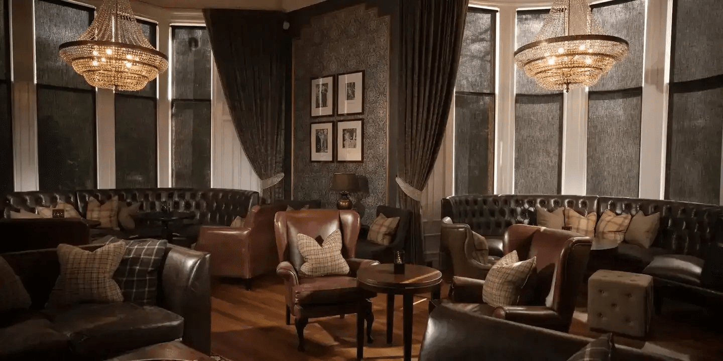 Dark lounge with leather Chesterfield sofas, tartan cushions and two crystal chandeliers.