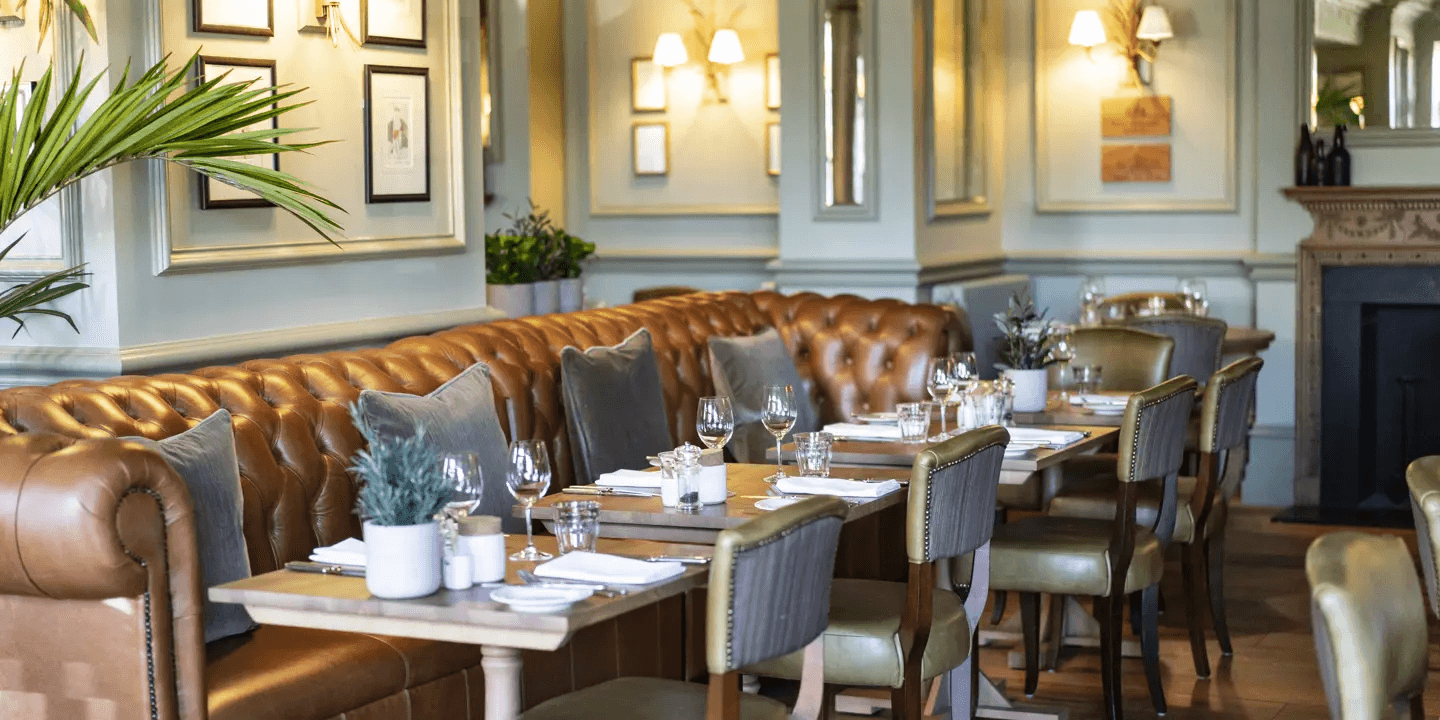 Restaurant dining room with tan leather banquette seating, laid tables and wall sconces at Hotel du Vin Harrogate.