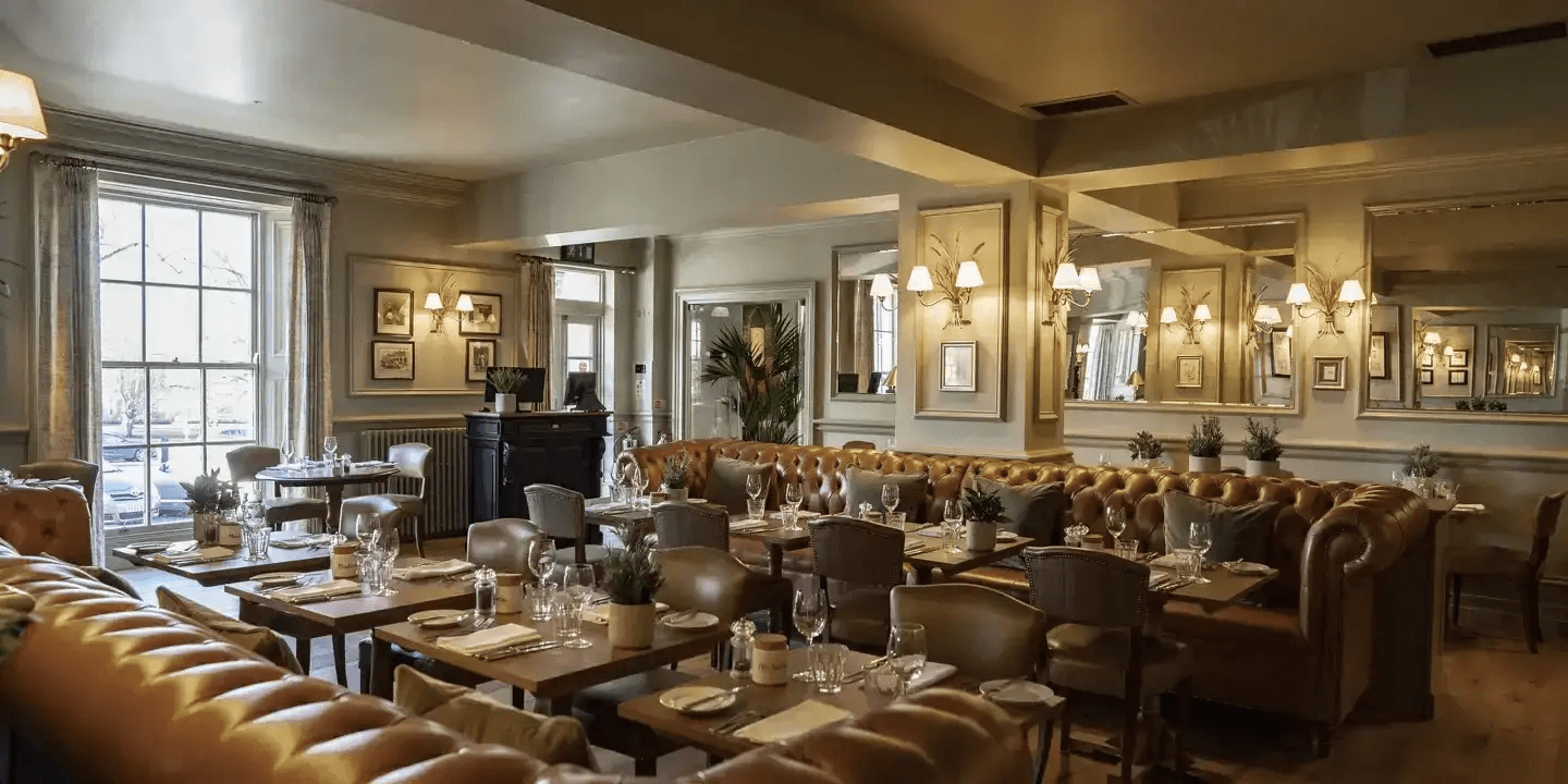 The restaurant interior with tan leather Chesterfield banquettes and laid dining tables.