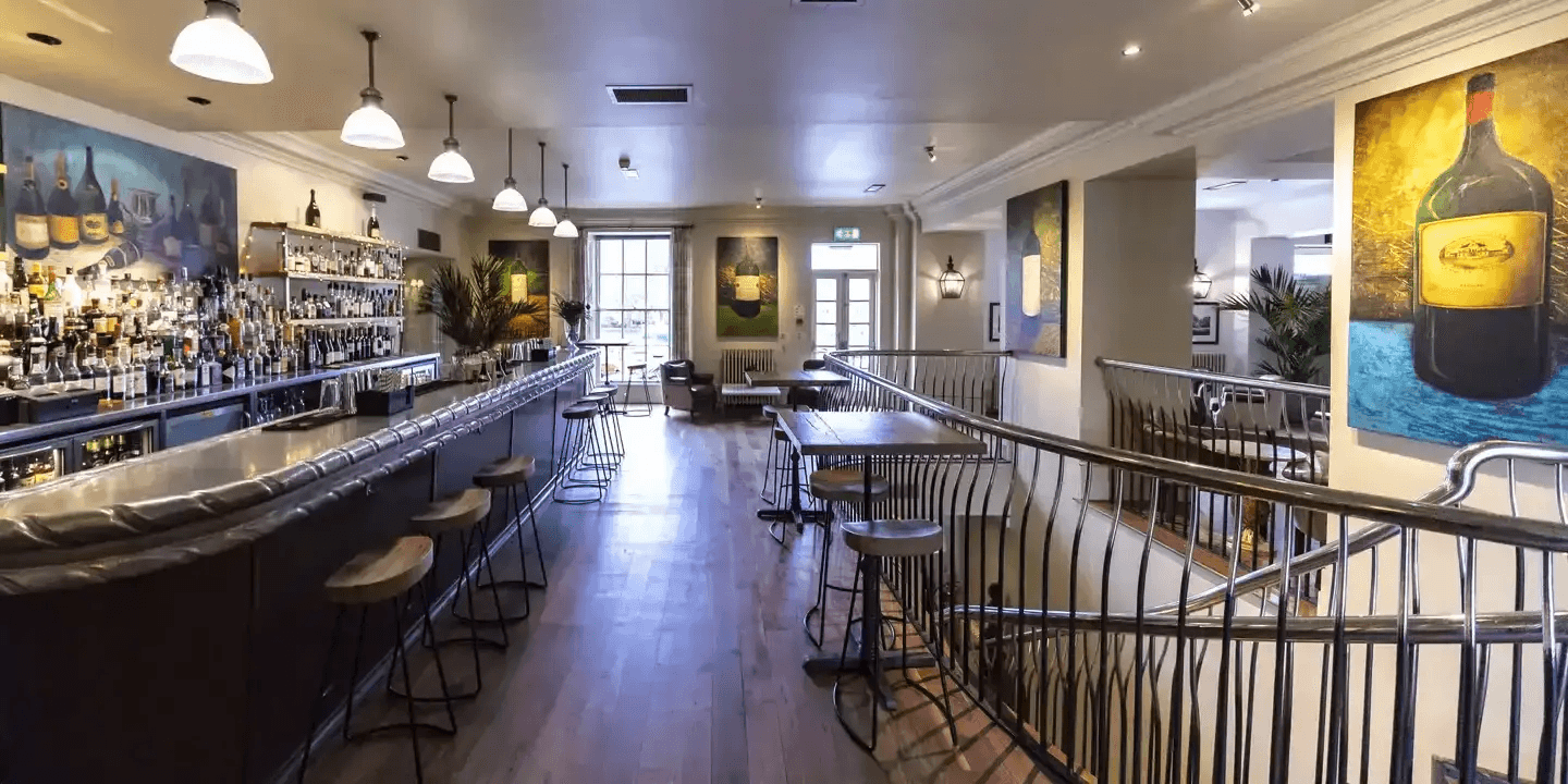 The long bar and high stools inside Hotel du Vin Harrogate with wine-themed artwork.