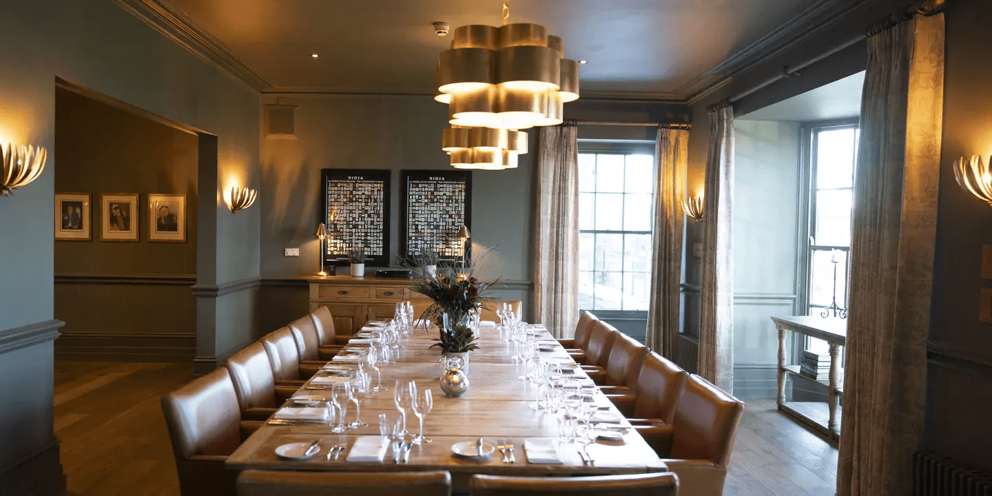 Private dining room with long wooden table, tan leather chairs and brass pendant lighting.