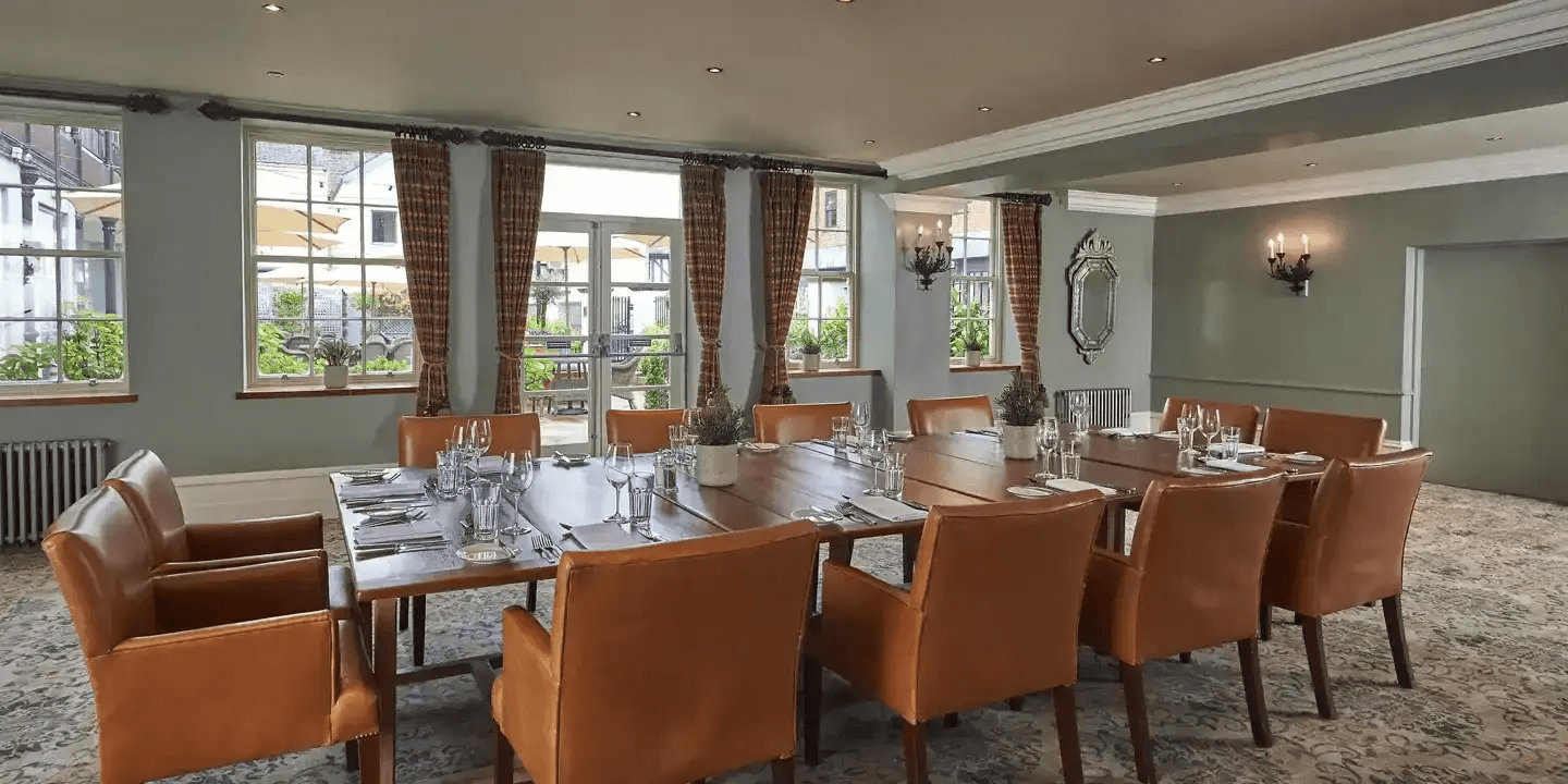 Private dining room with a long wooden table, tan leather chairs and garden views.
