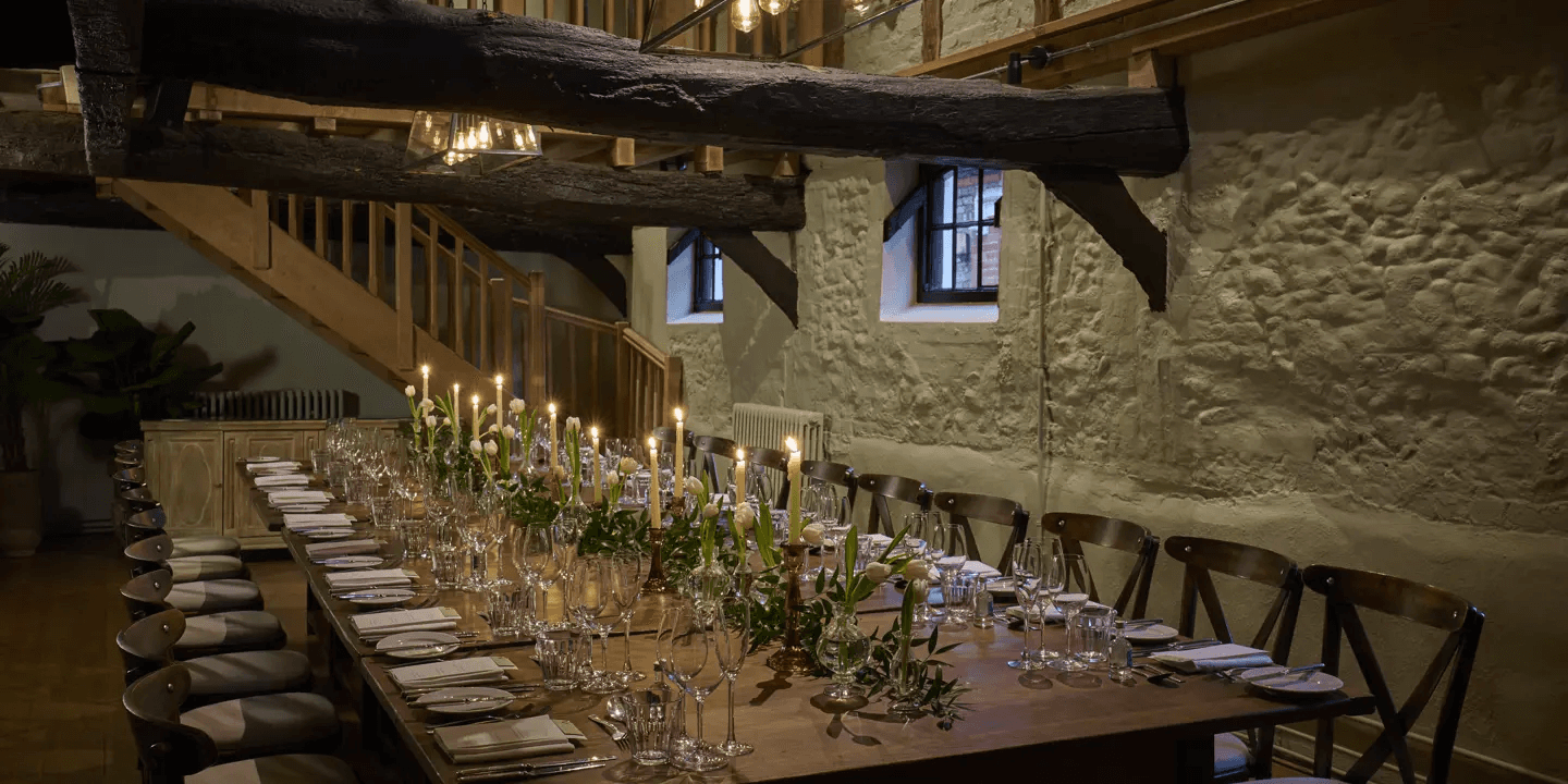 Long banquet table set with candles and white tulips in a stone-walled function room.