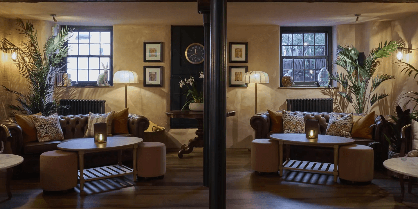 Dimly lit hotel lounge with leather Chesterfield sofas, floor lamps and palm plants.