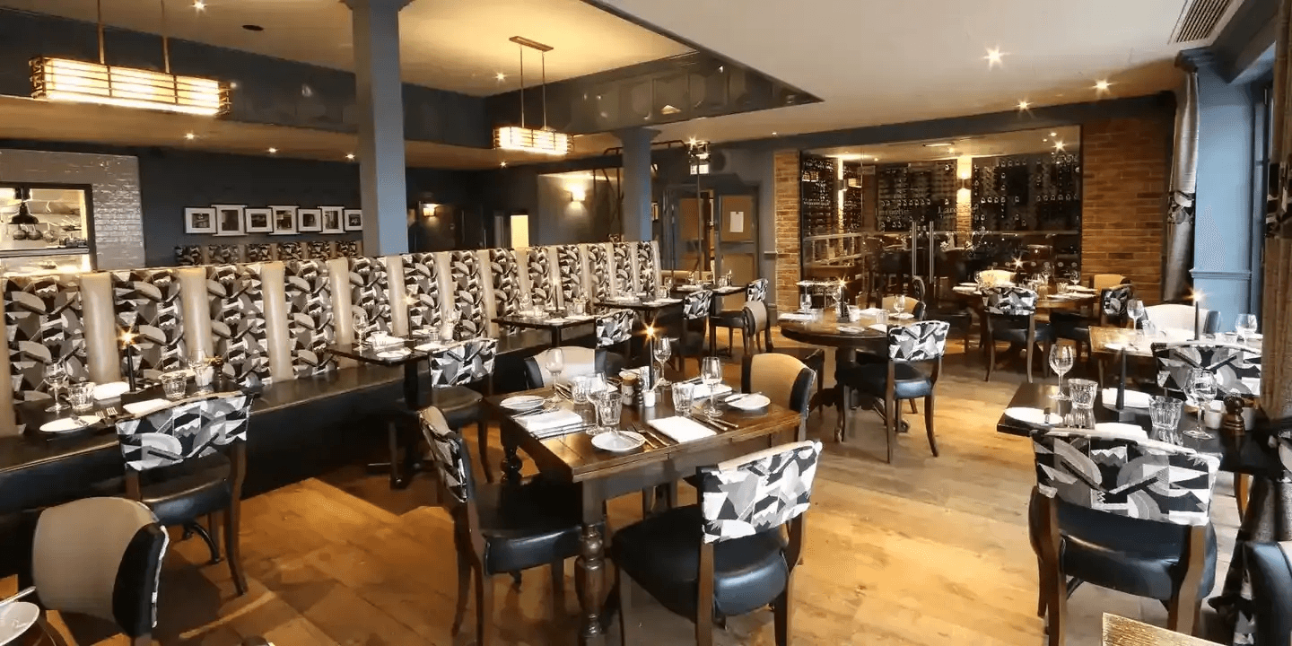 Candlelit restaurant dining room with dark wood tables, patterned chairs and a wine wall.