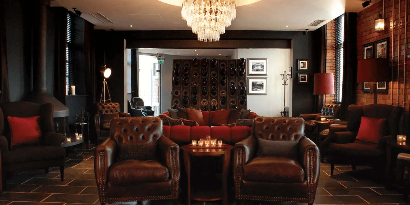 Dimly lit hotel lounge bar with leather Chesterfield armchairs and a crystal chandelier.