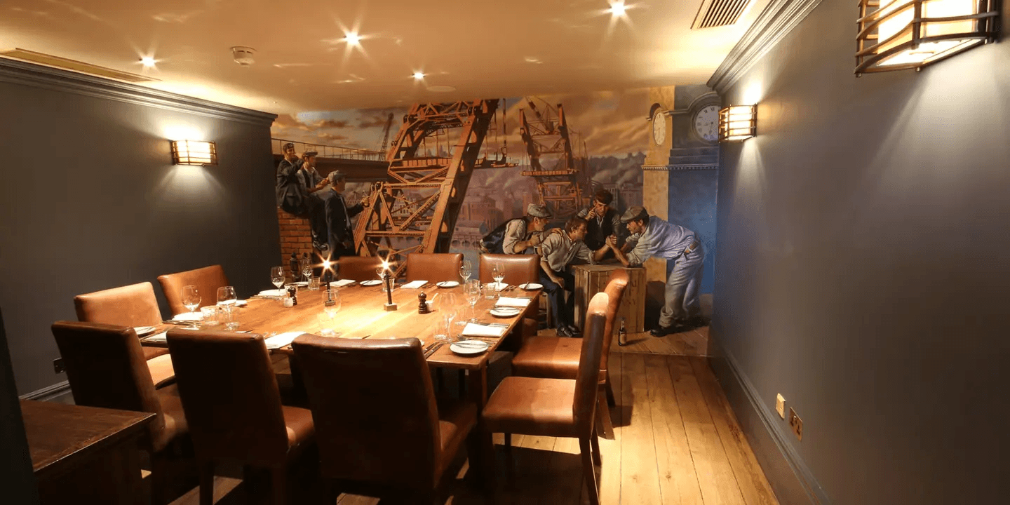 Private dining room with a long wooden table, leather chairs and a shipyard mural.