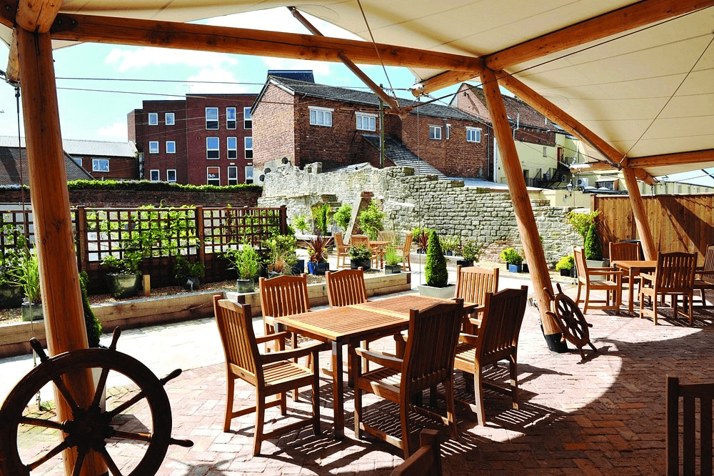 Sunlit terrace with teak garden furniture under a timber and canvas canopy.