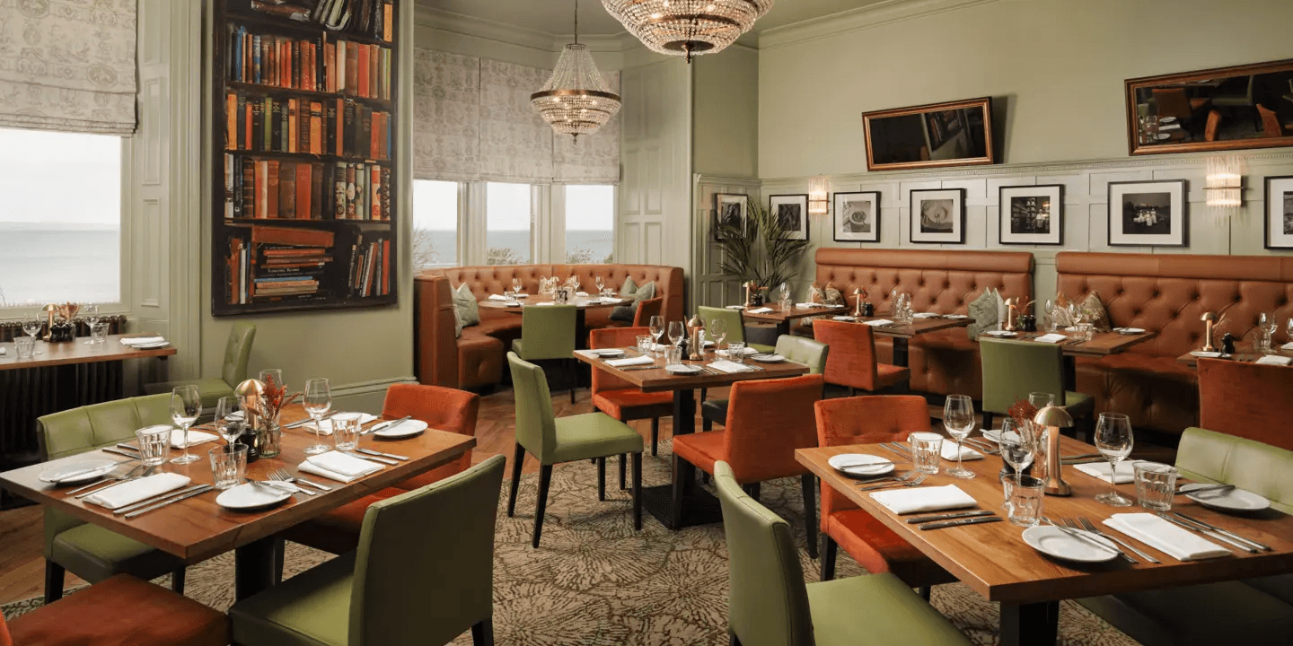 Restaurant interior with oak tables, green and terracotta chairs, leather banquettes and crystal chandeliers.