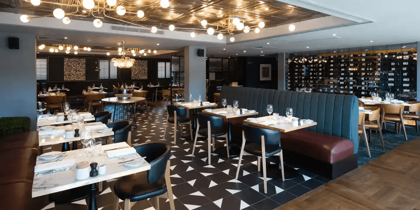 Restaurant interior with marble tables, tiled floor, booth seating and a large wine wall.