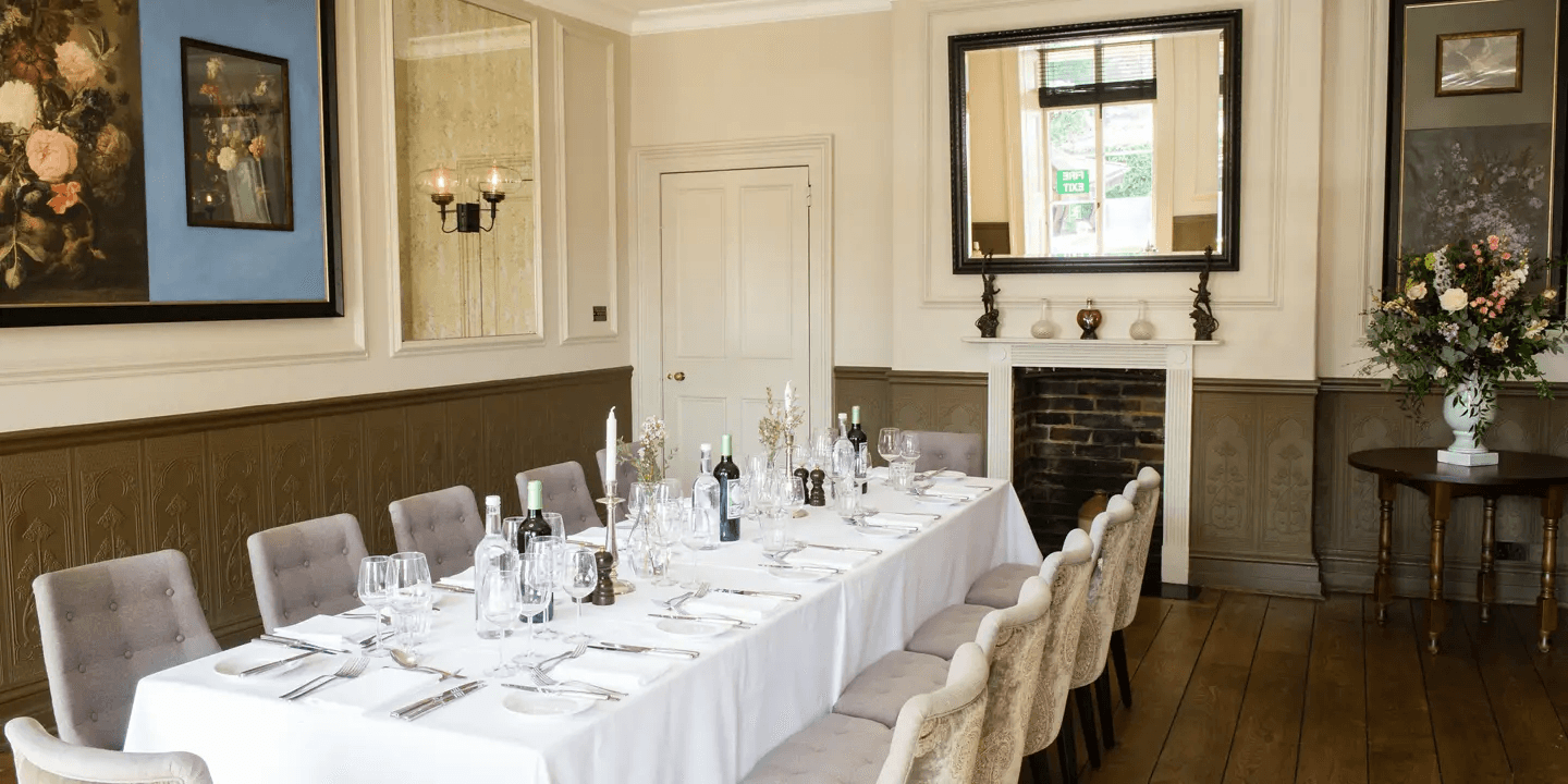 Private dining room with long white-clothed table, fireplace and grey upholstered chairs.