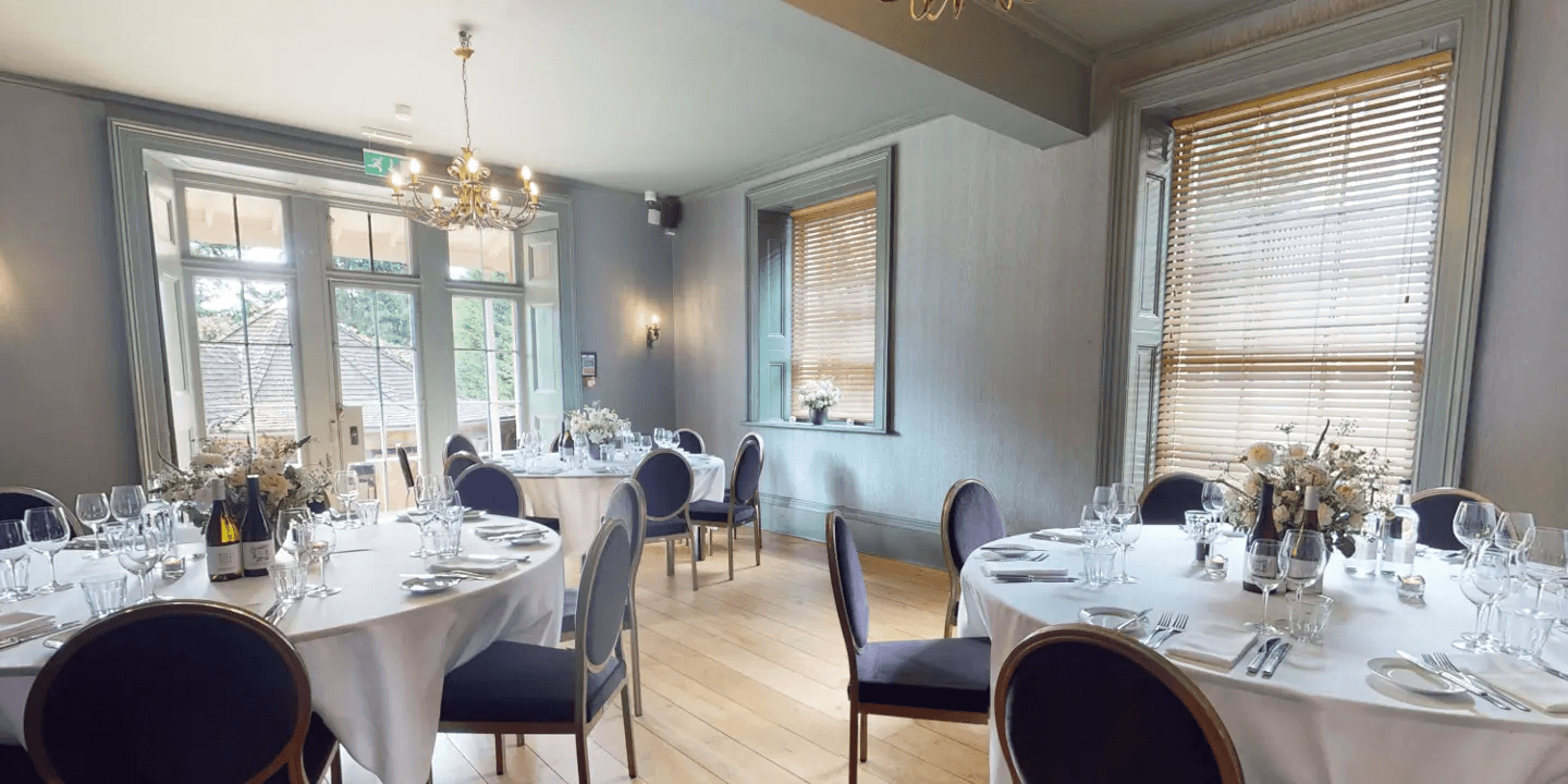 Private dining room with round tables, navy chairs and a gold chandelier.