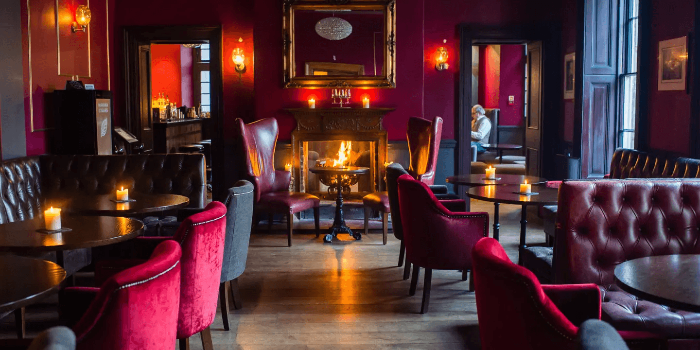 Candlelit bar lounge with crimson walls, velvet chairs and an open fireplace.